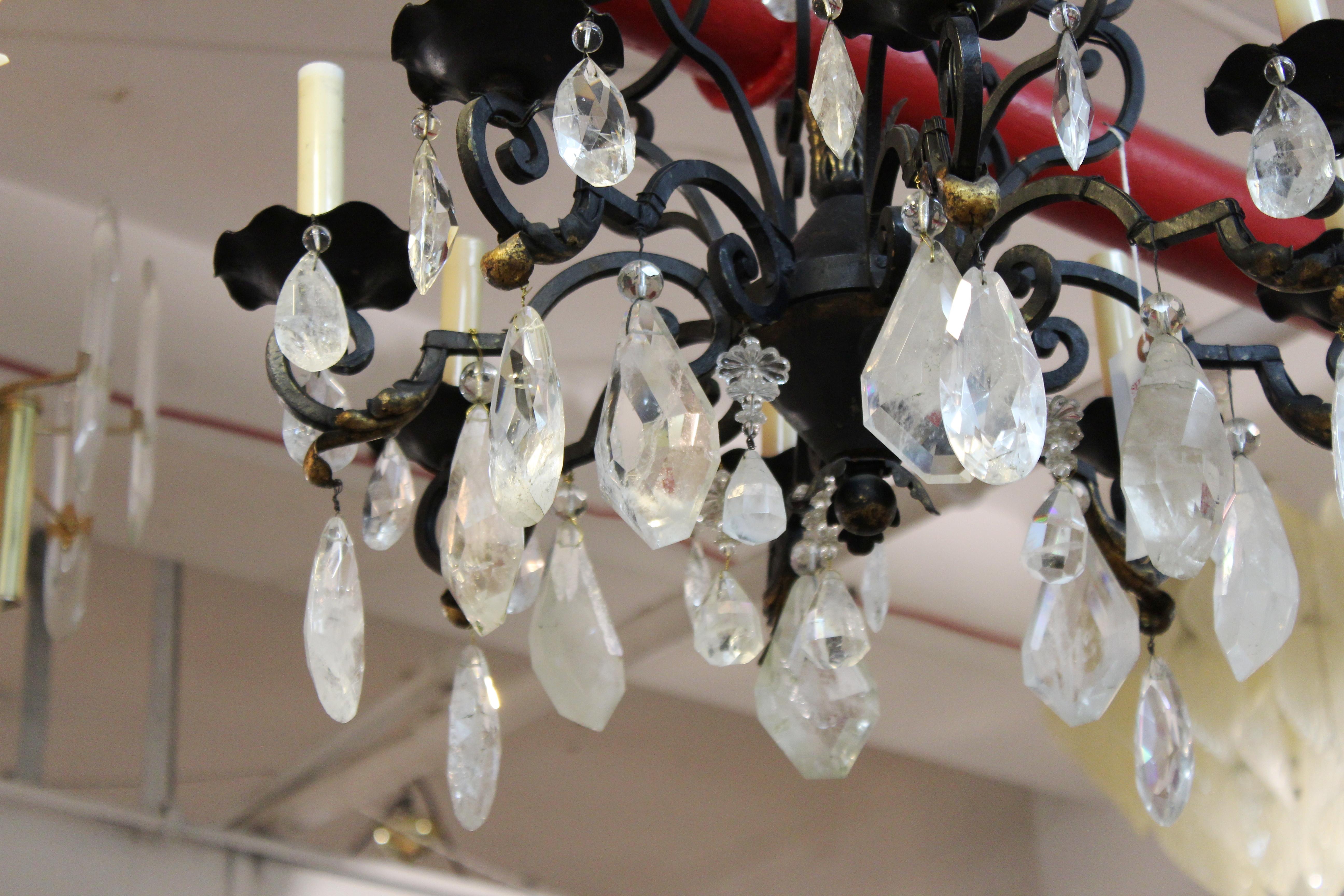 French neoclassical style bronze eight-light chandelier. The piece has hanging rock crystal quartz prisms and drops of various sizes and a decorative leaf motif on the frame. In great vintage condition with age-appropriate wear and use.