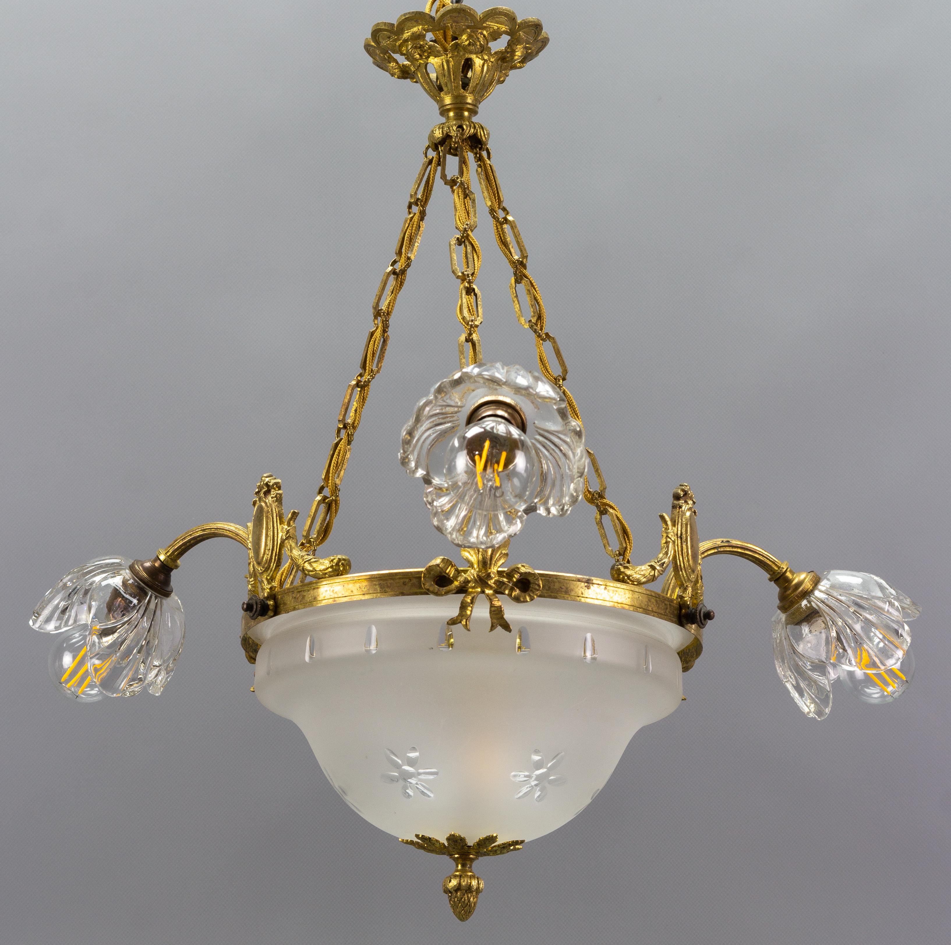 Französischer Kronleuchter im neoklassischen Stil aus vergoldeter Bronze und Glas mit vier Lichtern. Dieser schöne Kronleuchter hat drei Arme, die jeweils in einem blumenförmigen Lampenschirm aus klarem Glas enden, und einen schön geformten,