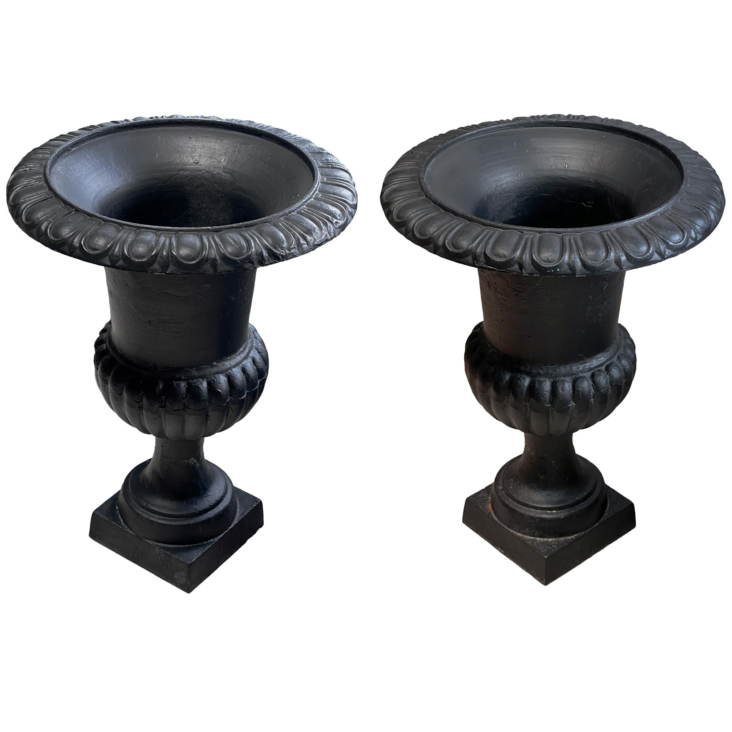 Pair of elegant vintage French Neoclassical-style cast iron urns or planters dating back to the early 20th century. These exquisite jardinières feature a sturdy construction with a delightful black coat with natural iron patina, perfect for a