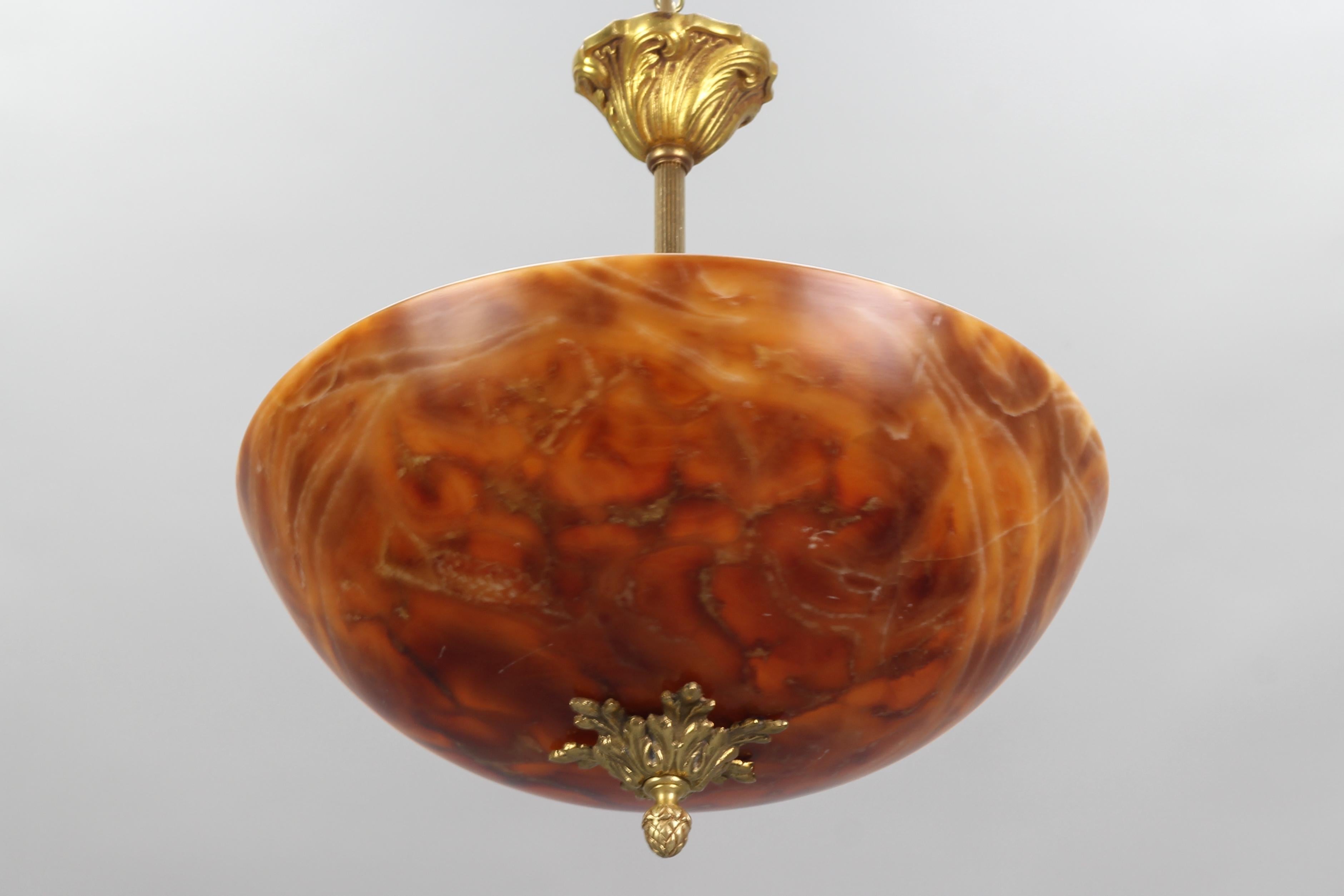Beautiful French Neoclassical style pendant light fixture from the 1950s. This adorable pendant light features an orange alabaster shade and an ornate central bronze finial. The light shining through the alabaster is warm and atmospheric and it