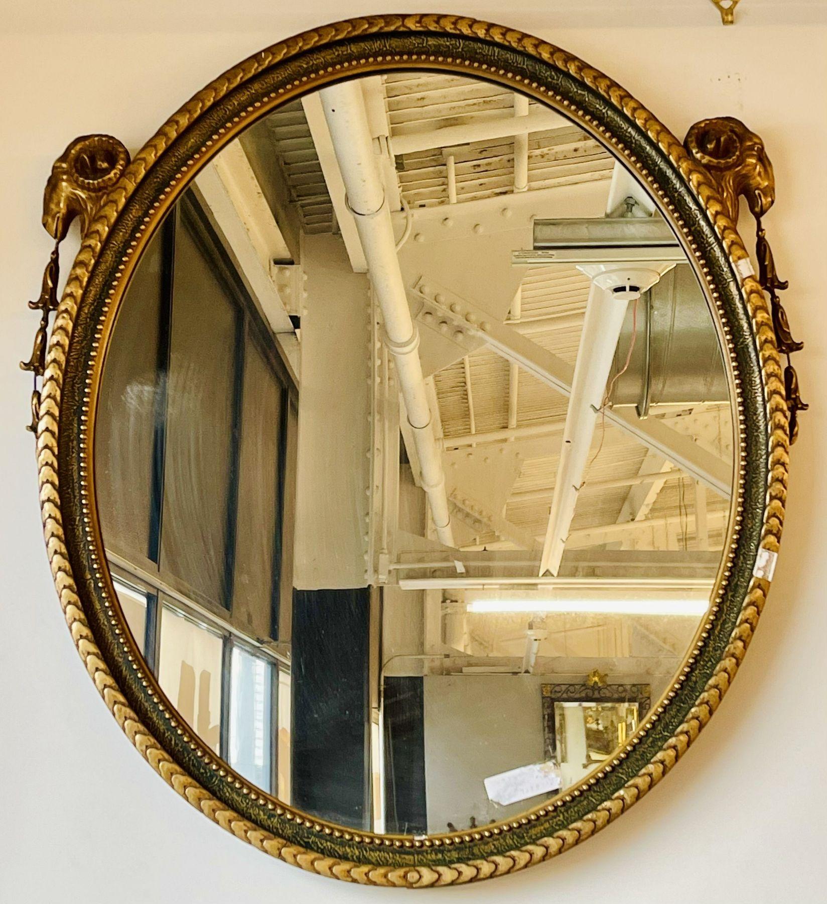 A beautiful French neoclassical style oval mirror with whimsical rams' heads design, circa 1950s, the oval glass surmounted in a painted and gilded frame decorated with annulated beadings, the top having a ram's head on each side.