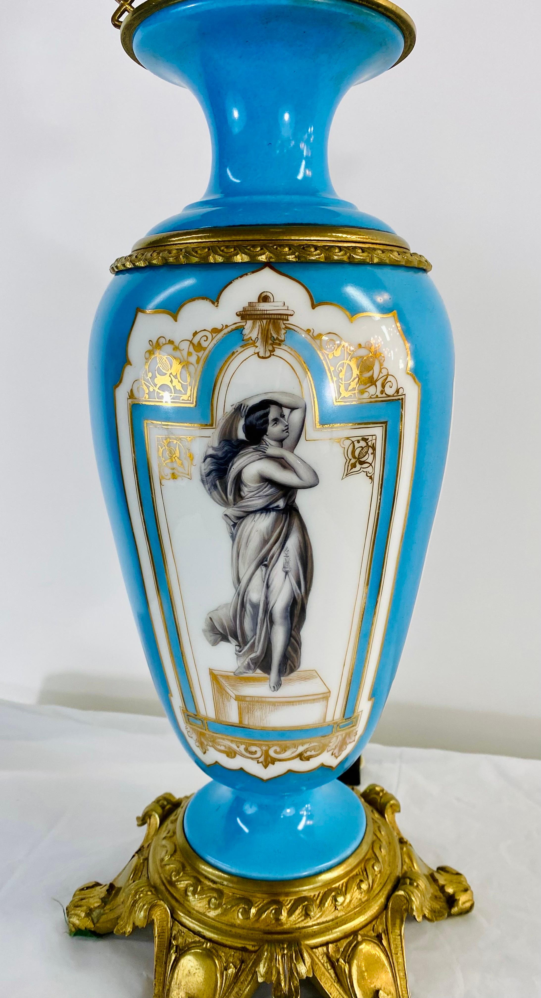 A pair of early 20th century French Neoclassical converted oil table lamps.  The lamps are made of porcelain and are beautiful hand painted featuring a woman portrait in the middle and  painted in white and blue. The elegant lamps are brass mounted