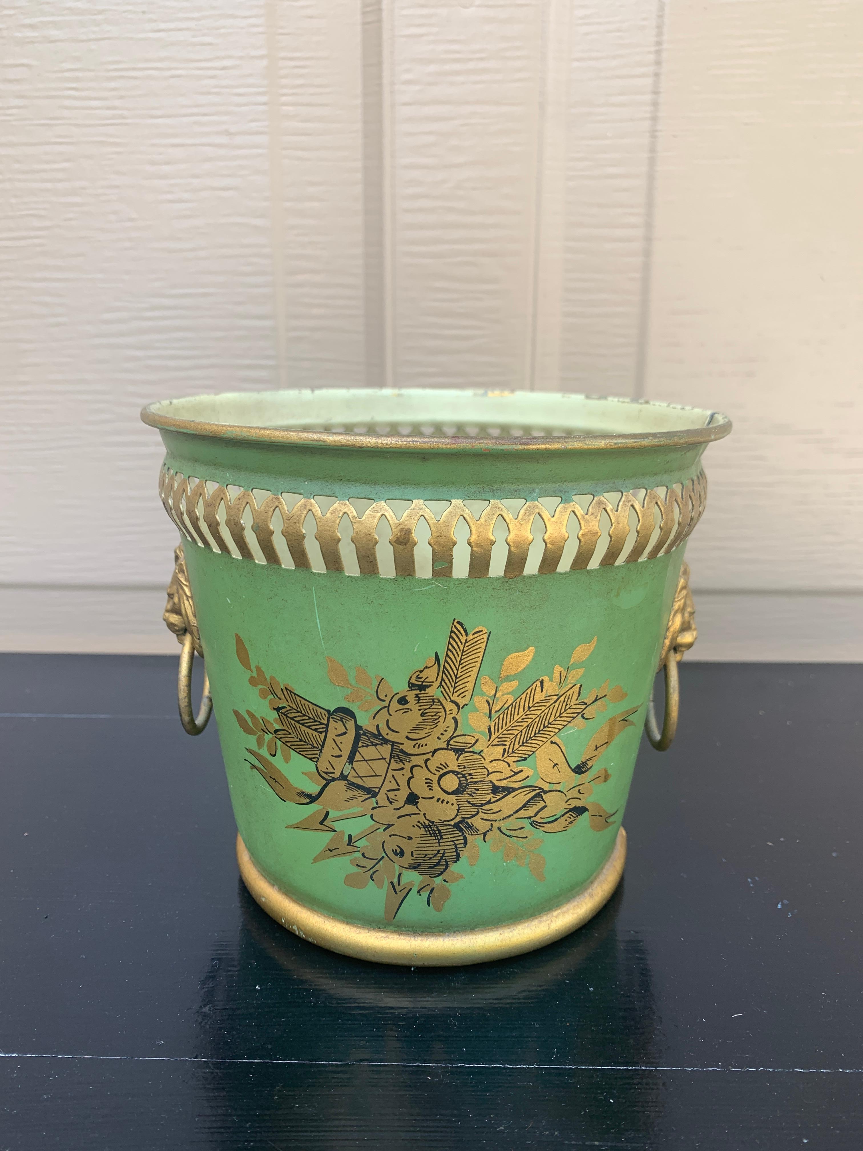 Precioso cacharro, macetero o jarrón neoclásico de tole verde y dorado con detalles pintados en la cabeza y cabezas de león de latón

Francia, circa principios del siglo XX

Medidas: 5,75