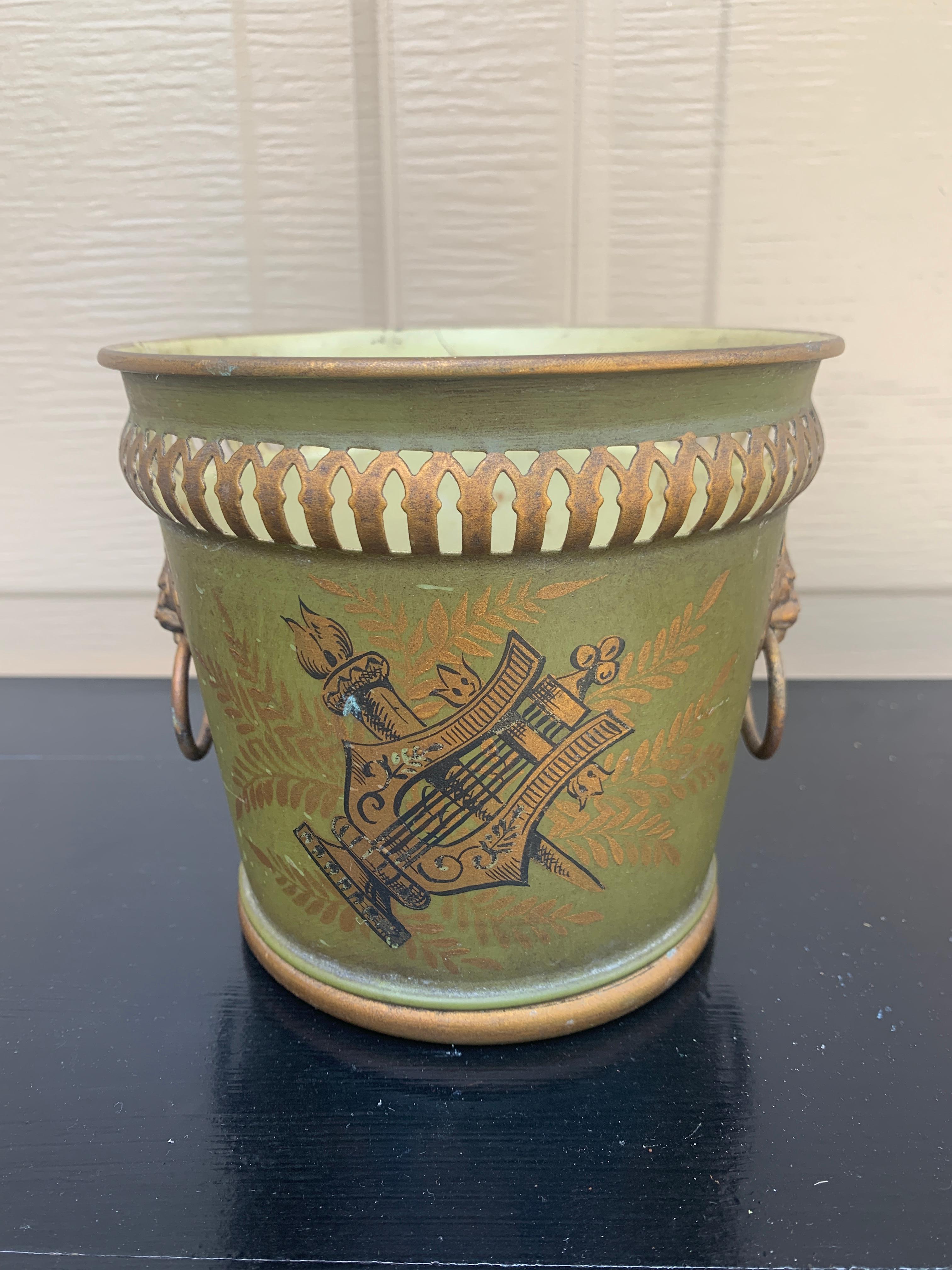 A gorgeous neoclassical green & gold tole cachepot, planter, or vase with head-painted details and brass lion heads

France, Circa Early 20th Century

Measures: 5.75