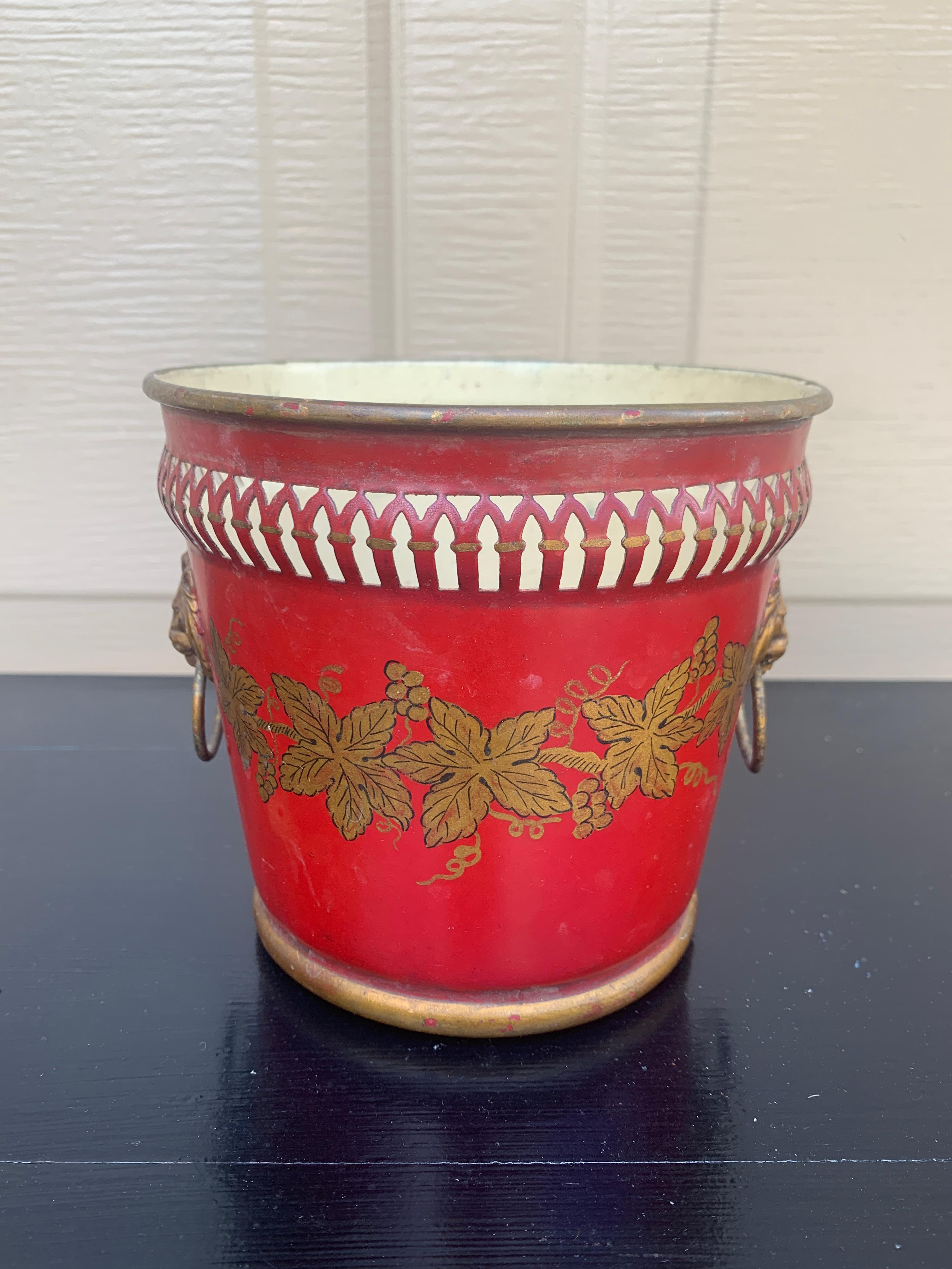 A gorgeous neoclassical red & gold tole cachepot, planter, or vase with head-painted details and brass lion heads

France, Circa Early 20th Century

Measures: 5.63