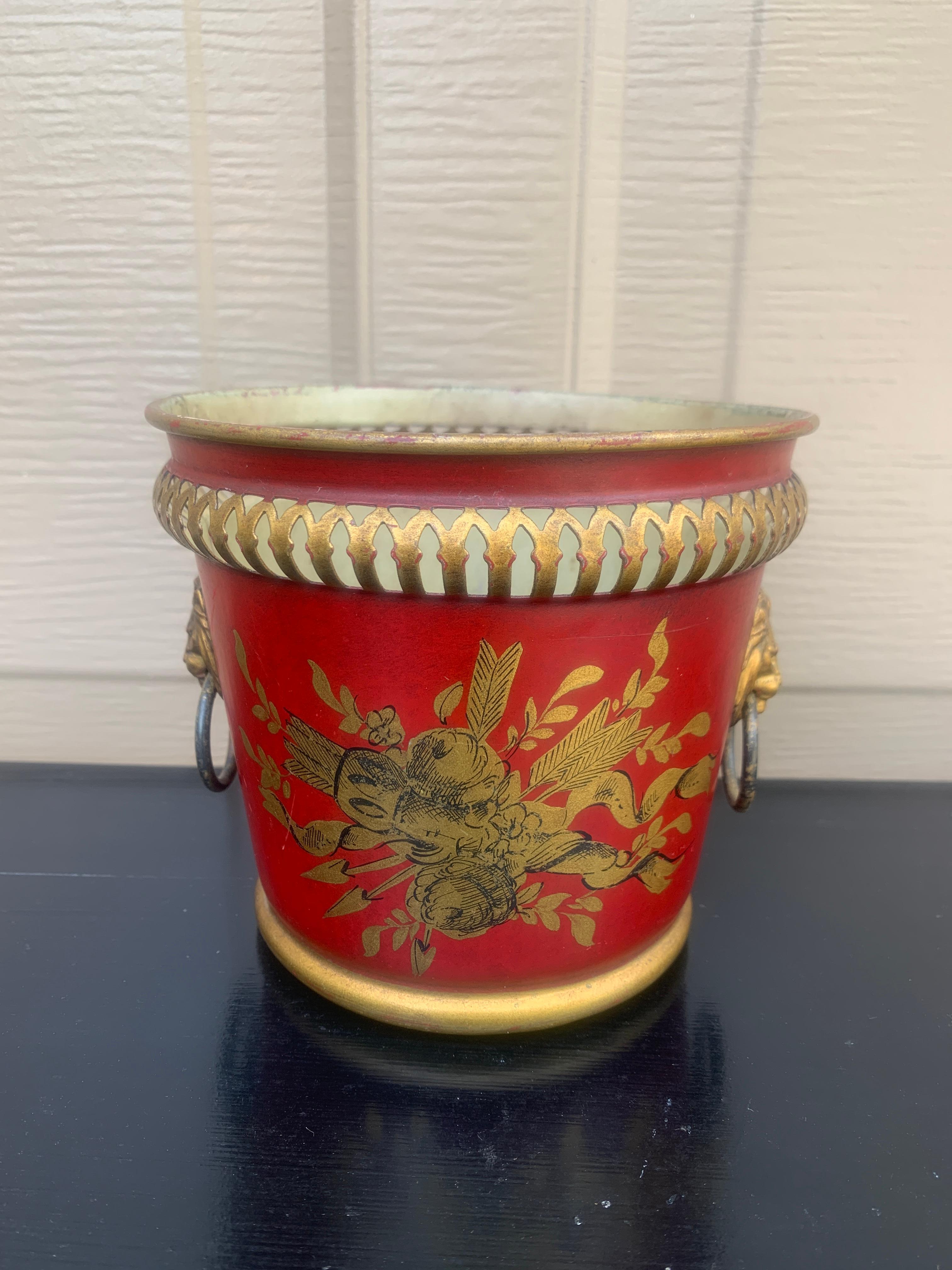 A gorgeous neoclassical red & gold tole cachepot, planter, or vase with head-painted details and brass lion heads

France, Circa Early 20th Century

Measures: 5.75