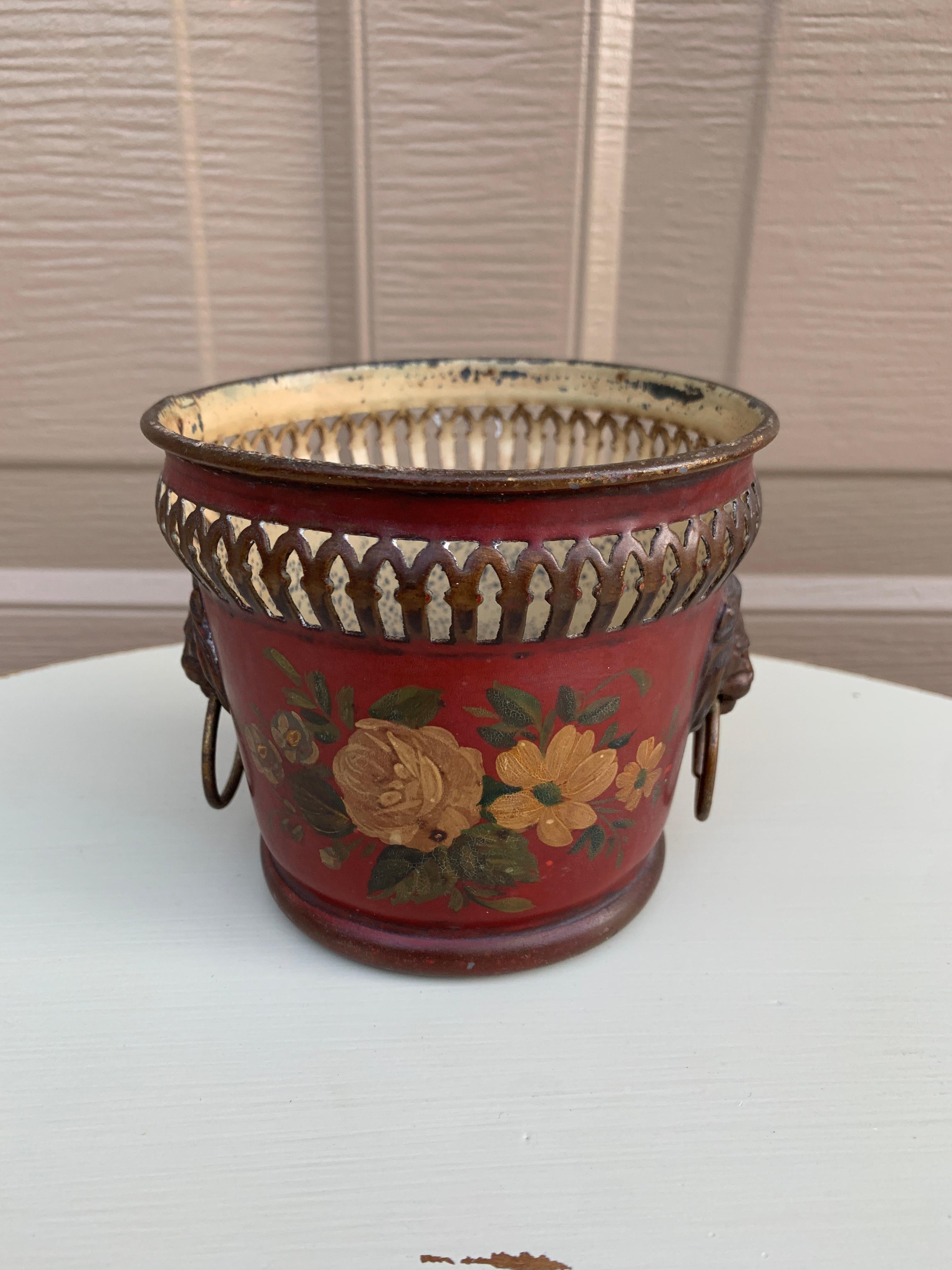 A gorgeous neoclassical red & gold tole cachepot, planter, or vase with head-painted floral details and brass lion heads

France, Circa Early 20th Century

Measures: 4.5