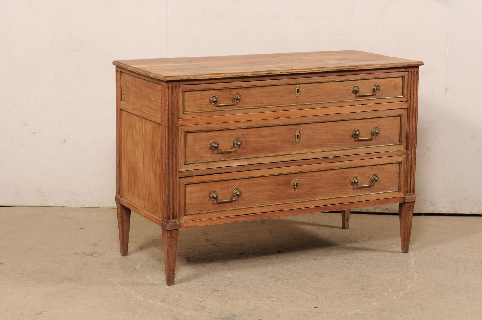 A French Neoclassical style three-drawer commode from the 19th century. This antique chest from France features a rectangular-shaped top which slightly overhangs the case below which houses three graduated drawers flanked within fluted side-posts,