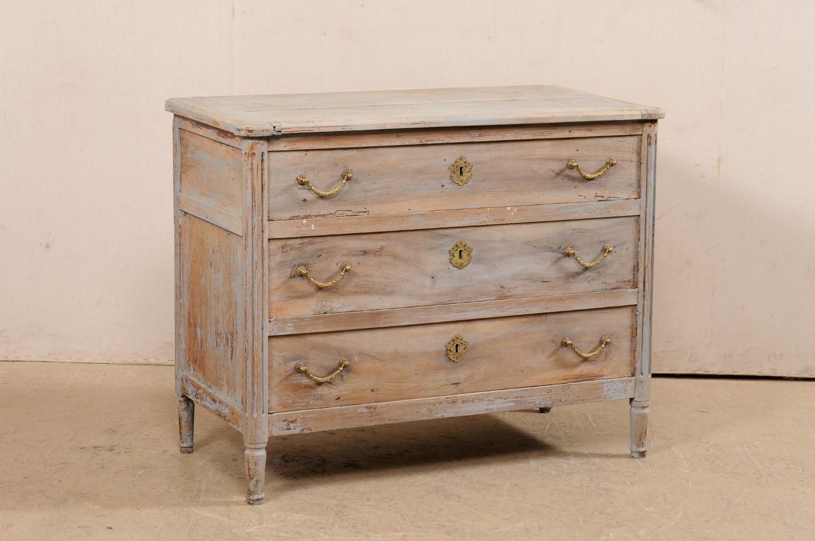 A French Neoclassic commode, with scraped finish, from the 19th century. This antique chest from France features a rectangular-shaped top with pronounced and rounded corners, which rests atop a neoclassical style case which houses three graduated