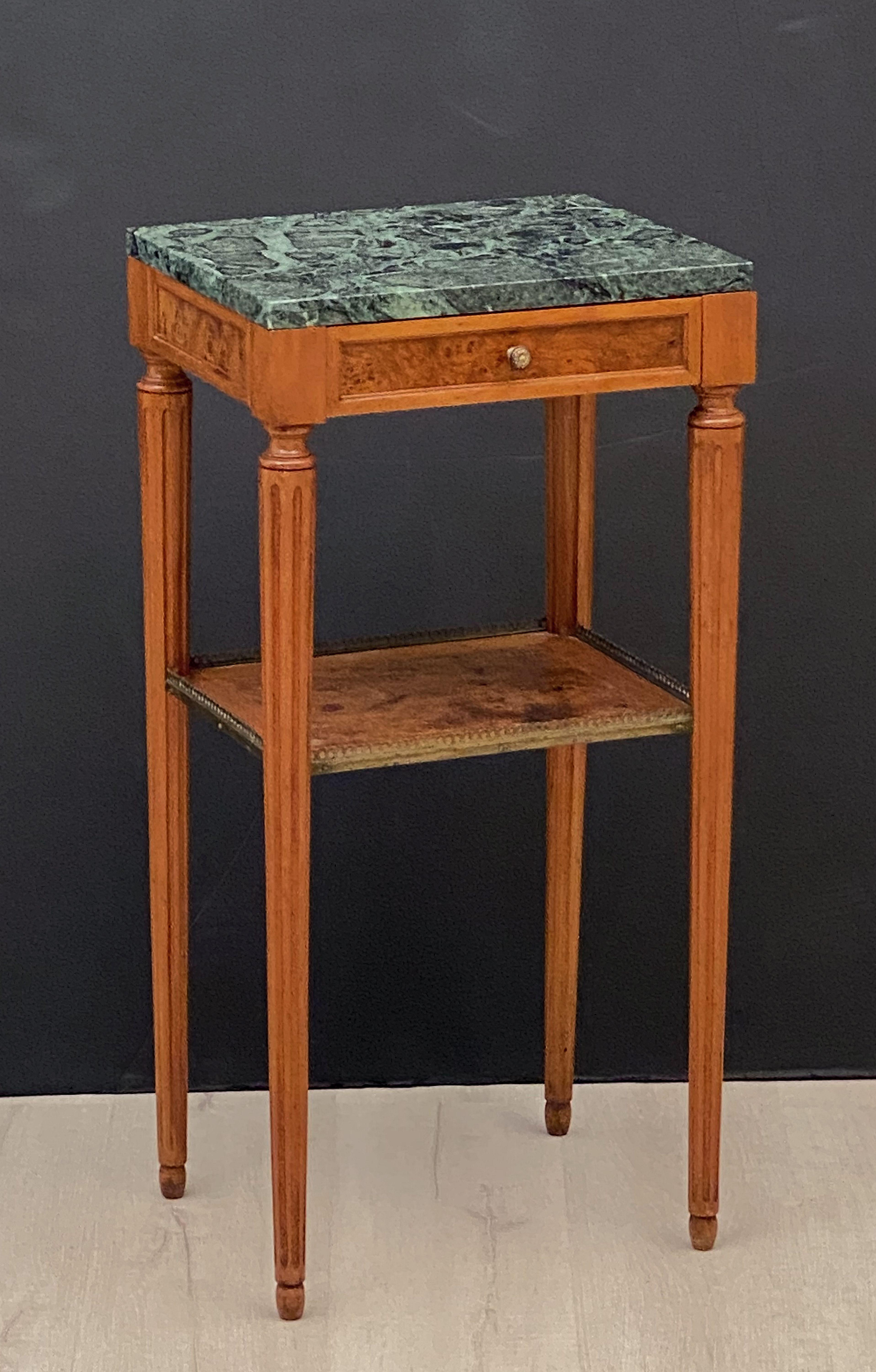 A fine pair of French bedside end tables or nightstands, each rectangular stand featuring a figured marble top over a frieze with one drawer, the drawer with decorative brass knob pull and burled wood accents, over a bottom tier of inlaid wood with