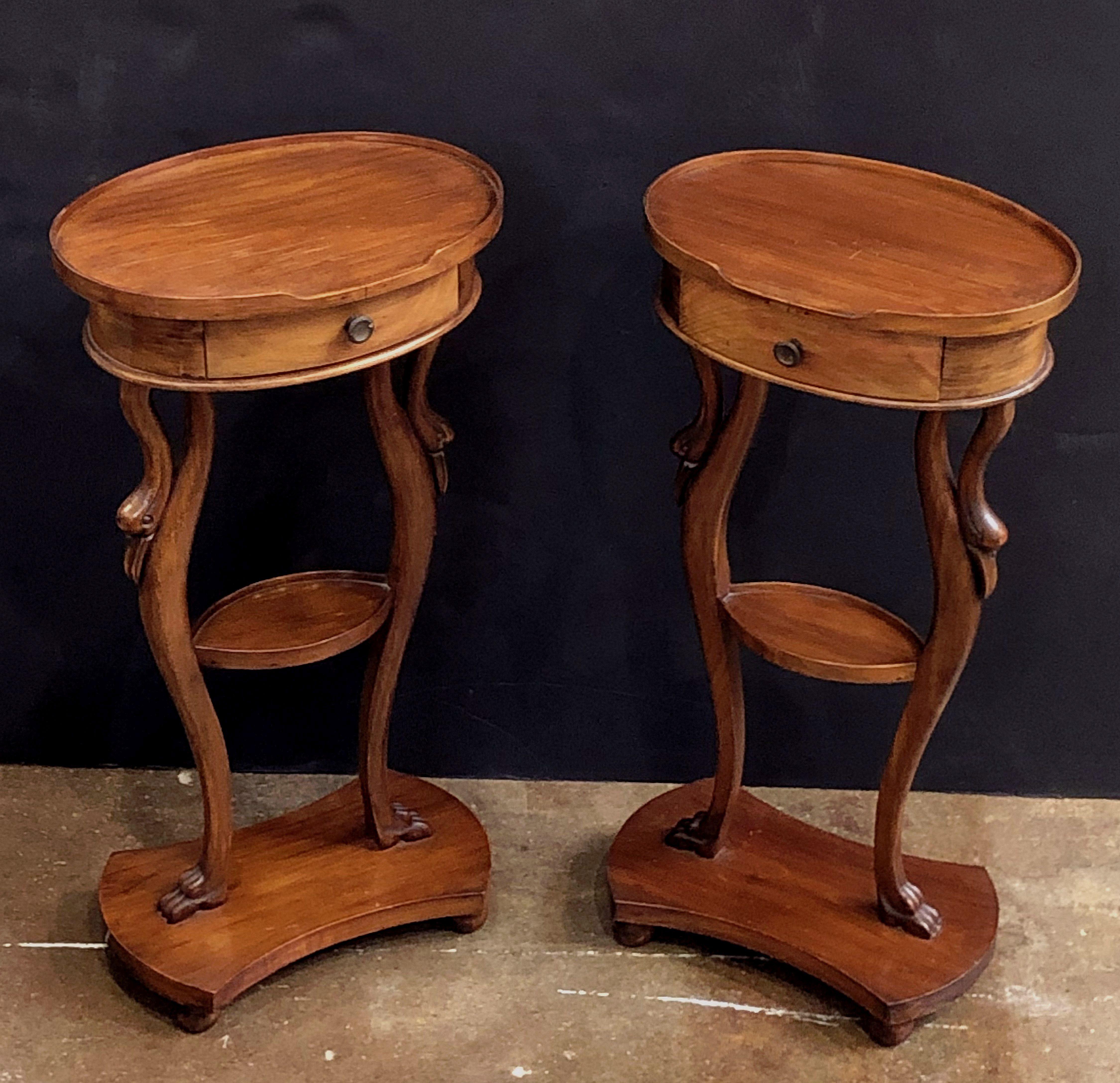 A pair of fine French nightstands or bedside end tables of mahogany, each with an oval top with gallery surround over a shaped frieze with a drawer, set upon a turned leg support with shelf, the support featuring a design of swans, over a small