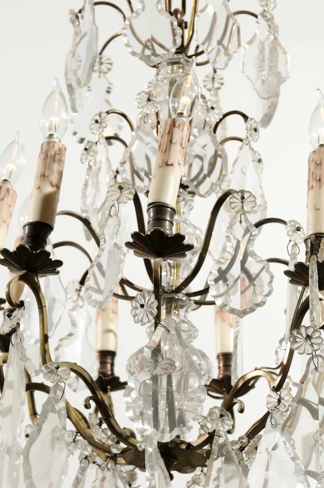 A French nine-light crystal chandelier from the early 20th century, with brass armature and flower-shaped bobèches. Born in France during the Belle-Époque era, this exquisite chandelier features a brass scrolling armature, adorned with large