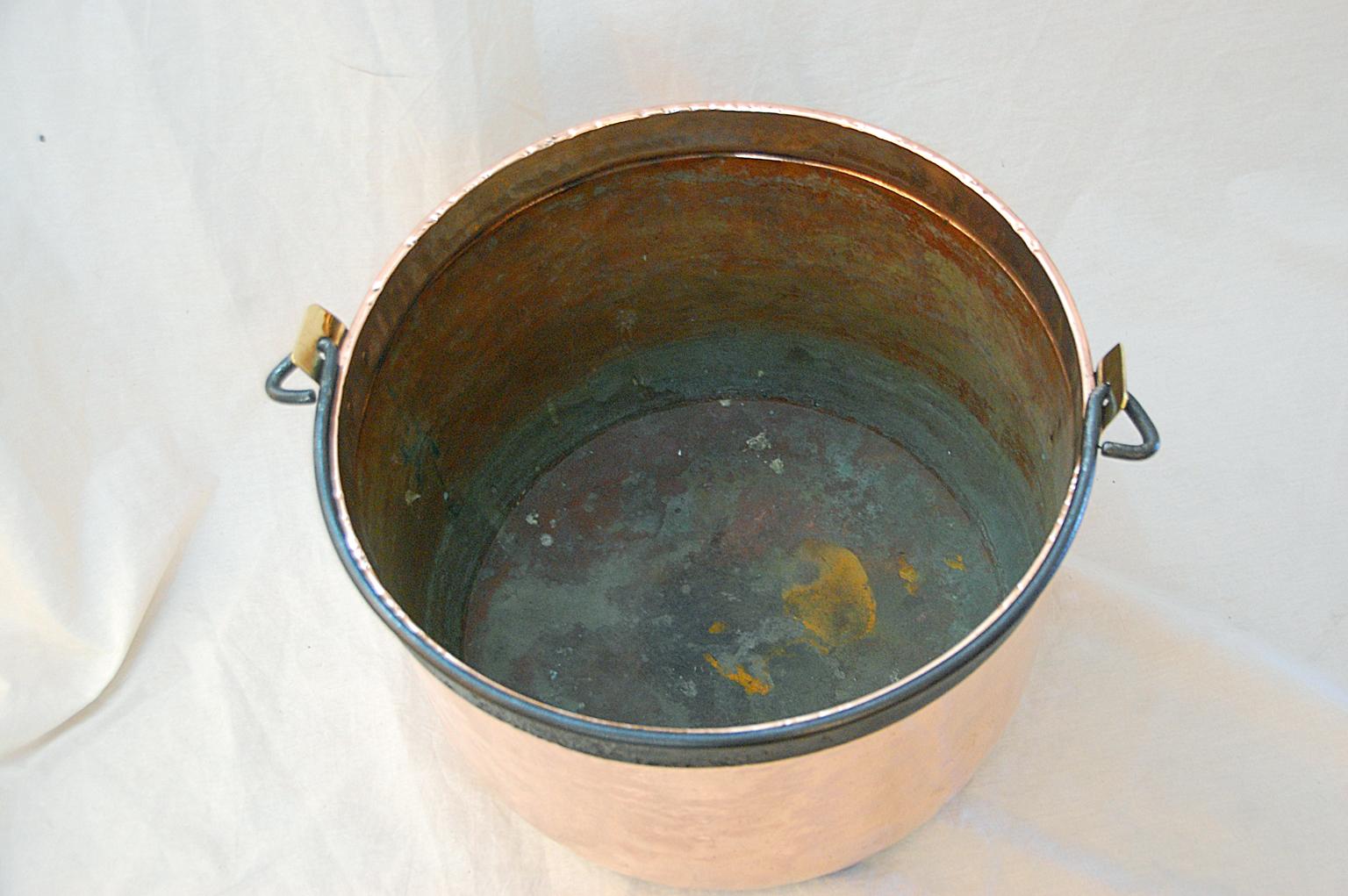 French nineteen inch copper cauldron with dovetailed and hammered construction, iron rim and wrought iron swing handle. There is a makers mark on the brass handle carrier 
