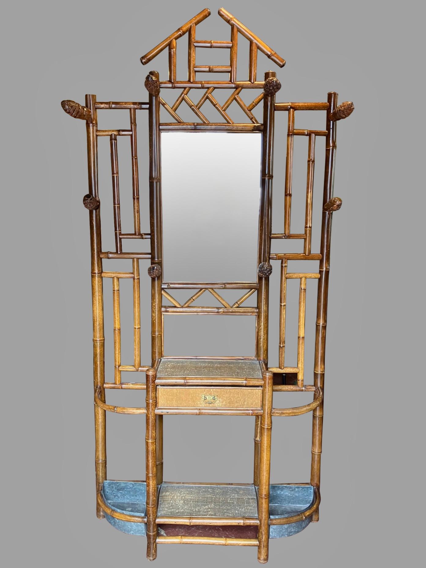 A stylish French late 19th century hall tree, the painted bamboo structure  of architectural form, with a central triangular pediment over 8 hat racks in the shape of pinecones. The center retains its original mirror above a rush covered platform