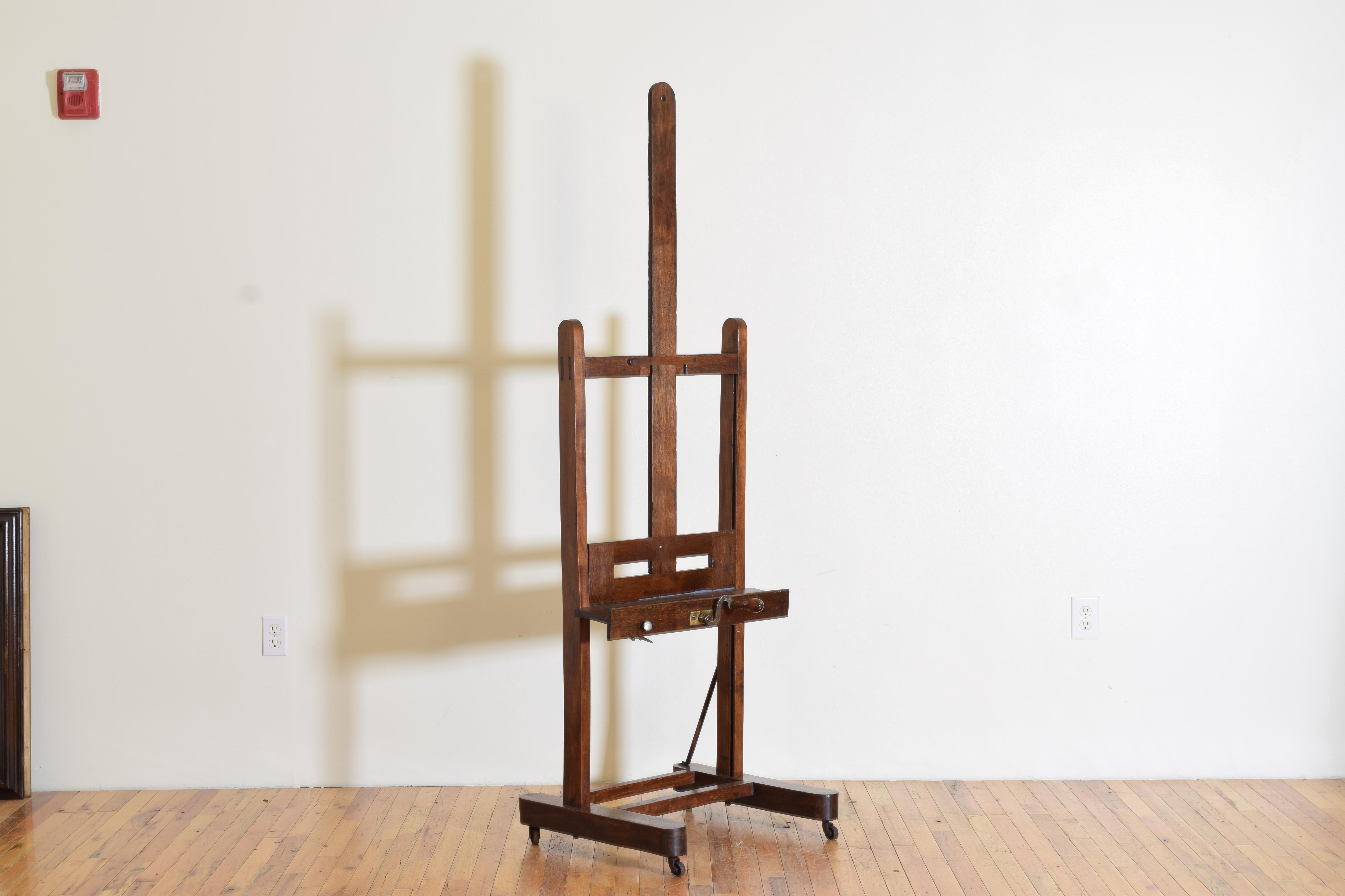 Height listed as shown in photographs but the easel is adjustable both up and down, having a tray to secure the canvas, original wooden crank handle, and casters at base, lacking one iron support rod.