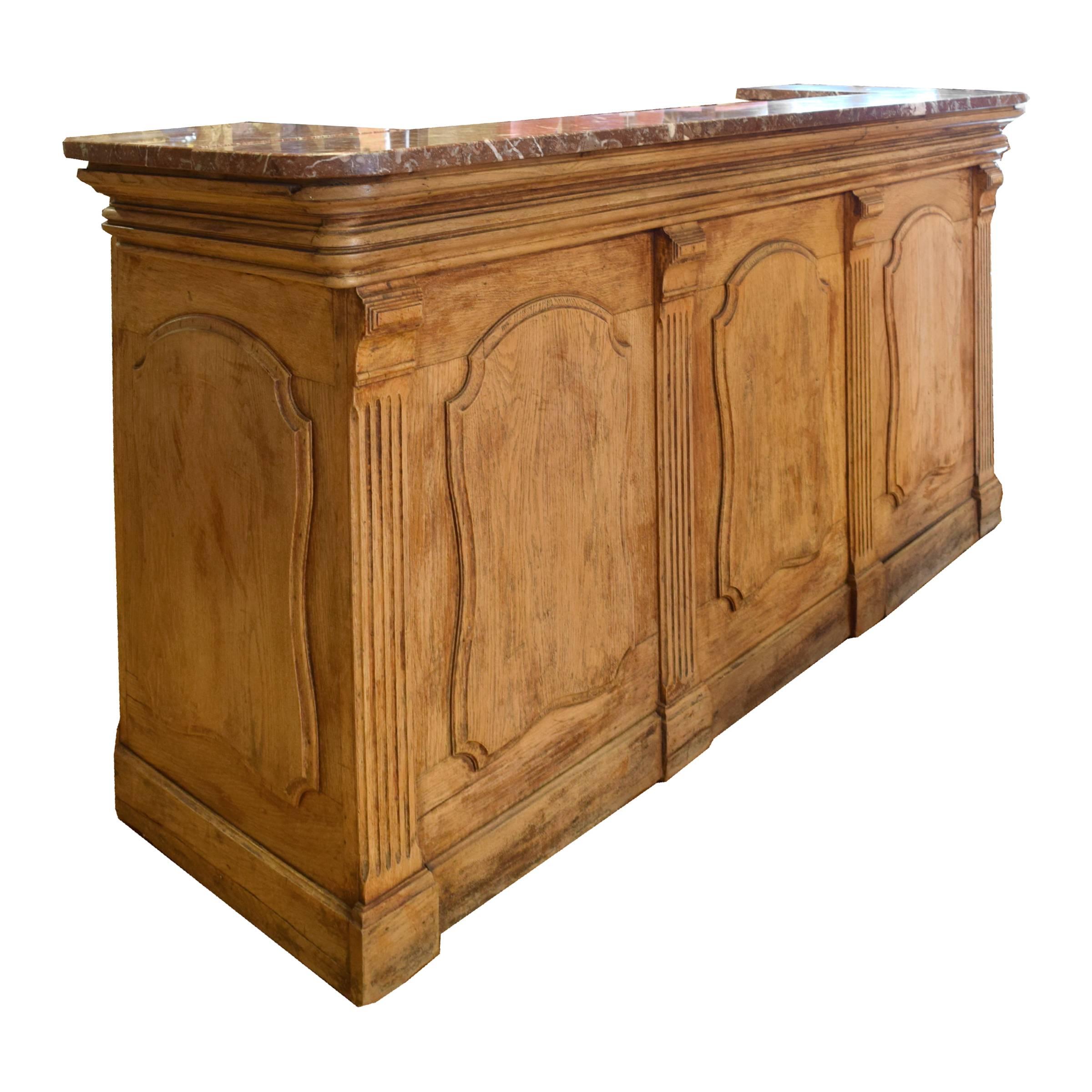 A great French oak desk or bar, from a Paris cafe, with panelled front and sides and a rose red marble top and surround, circa 1920.