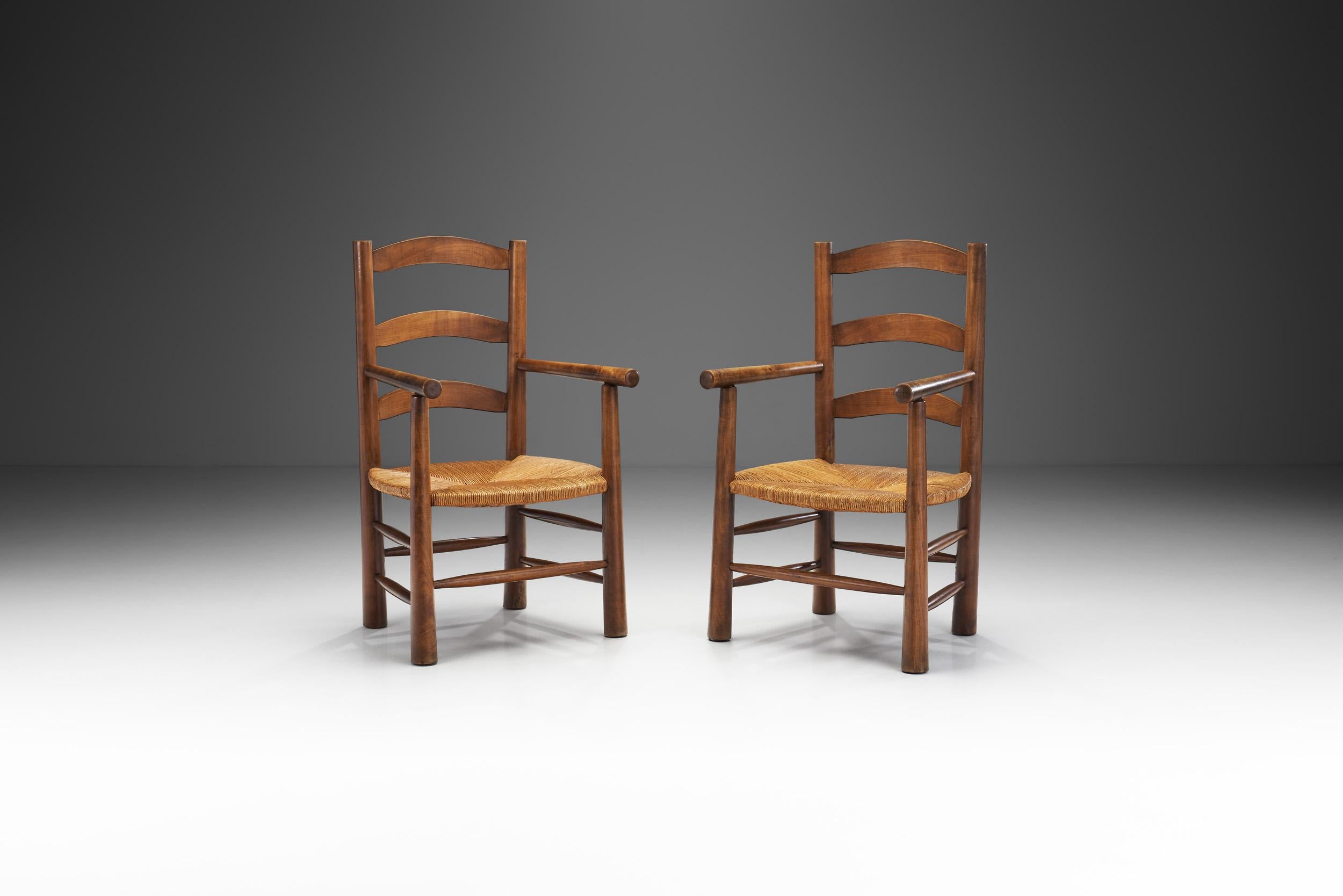 Cette paire de fauteuils rustiques a été réalisée dans les années 1950 en France, en s'inspirant des créations en bois et en paille de Charlotte Perriand. L'association de la structure en chêne et du siège en jonc tressé est un mélange organique et