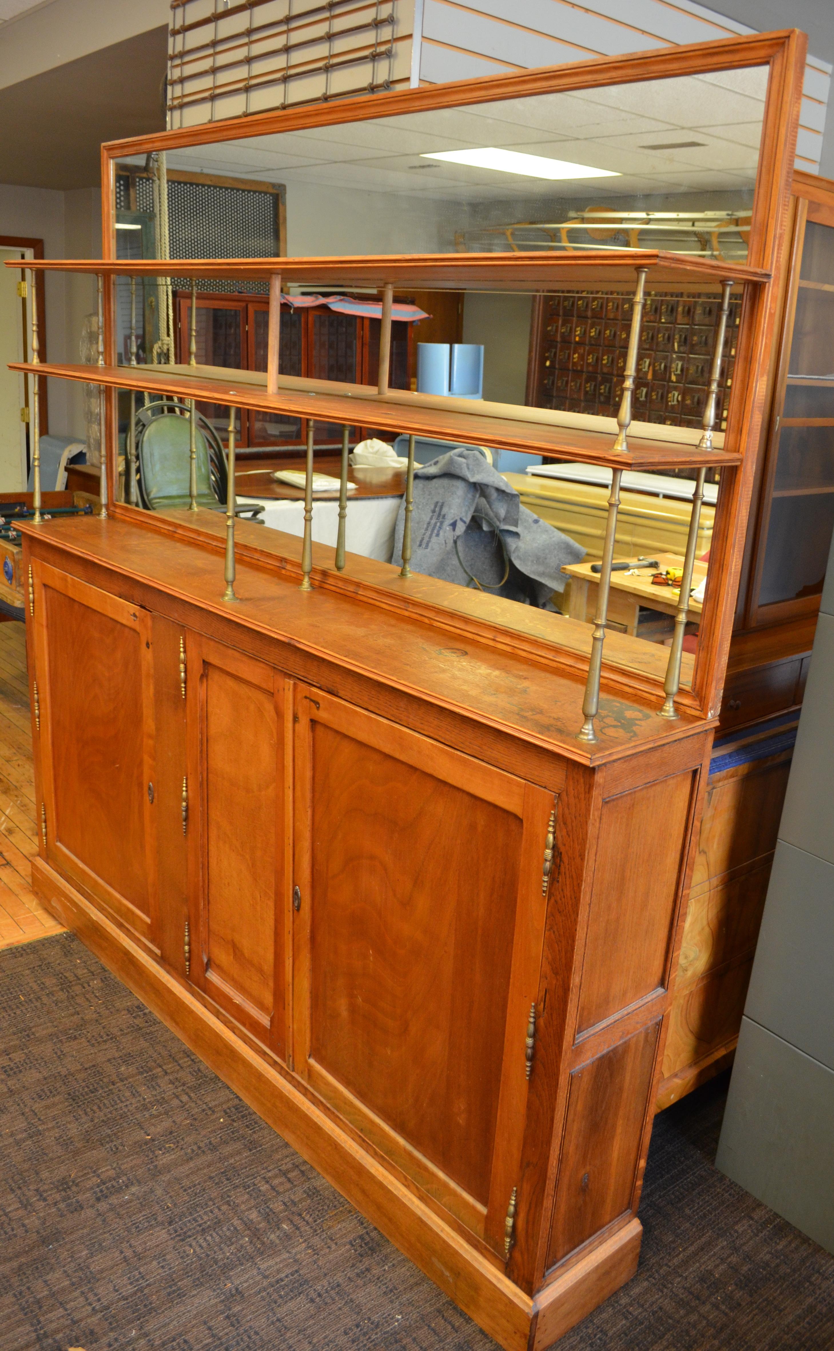 Back bar of oak from France, circa 1910. Two upper shelves are supported by brass spindles and backed by a plate glass mirror. Three lower doors open on storage area with one built-in shelf. Striking piece with antique French provenance only 12