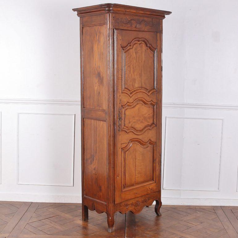 A French country bonnetiere, or single-door armoire, with nicely shaped paneled door, delicate carving in the top and base, and striking brass hinges and keyplates. A country piece of mixed woods - the case is solid oak and the door is cherrywood.