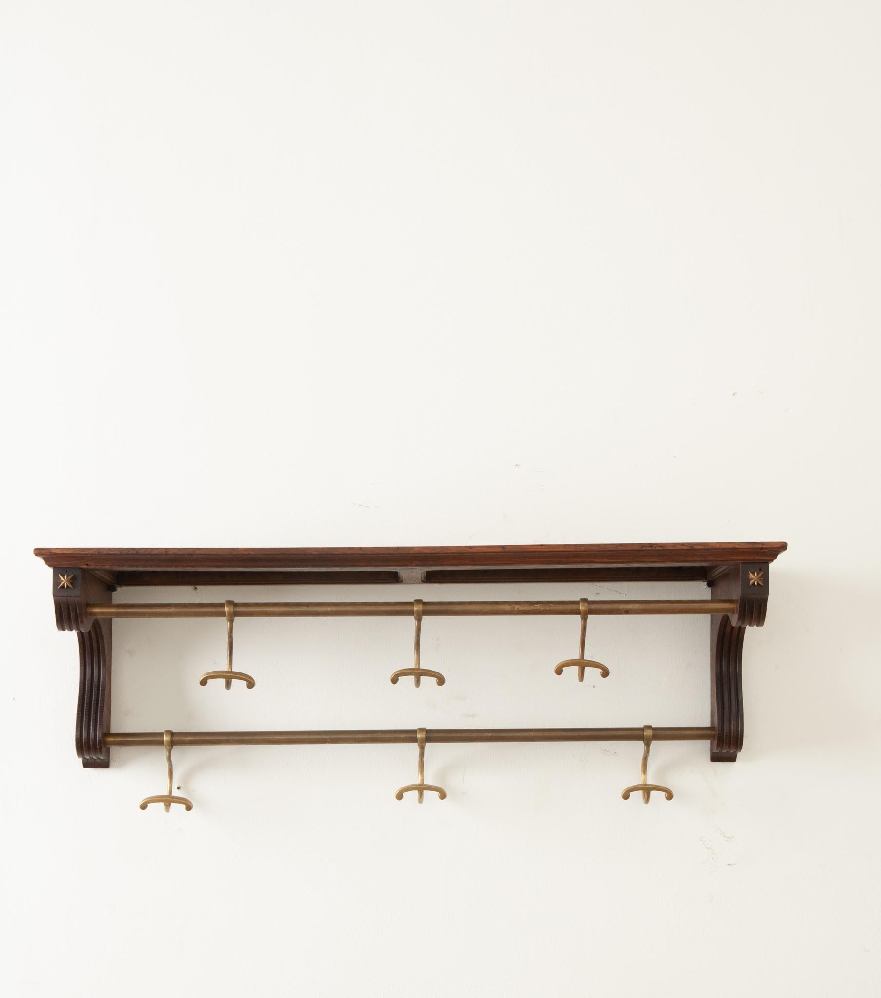 A French early 20th Century oak and brass train rack is the perfect shelf by your door or in your bathroom. The 9 ¾” top shelf is made of cane and is deep enough for hats or towels. There are six slidable hooks for hanging coats or towels. Be sure