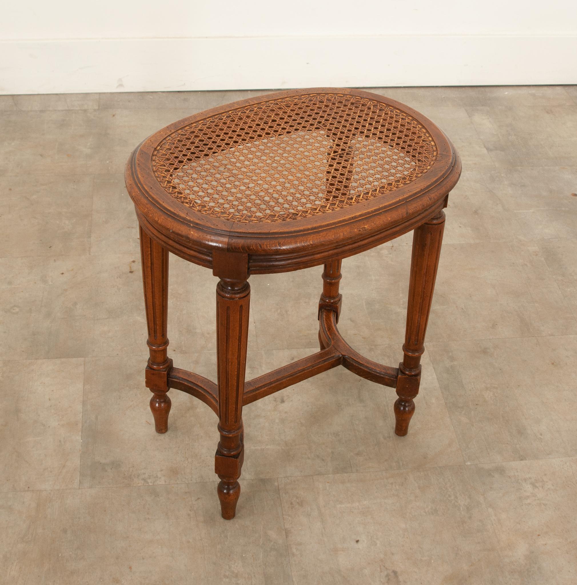 A French 19th century Louis XVI style hand-carved oak stool with cane top. Its oval top with a smooth, molded and trimmed edge holds original and perfect caning, and  it showcases the lovely rich tone of the well patinated oak. The top sits on a