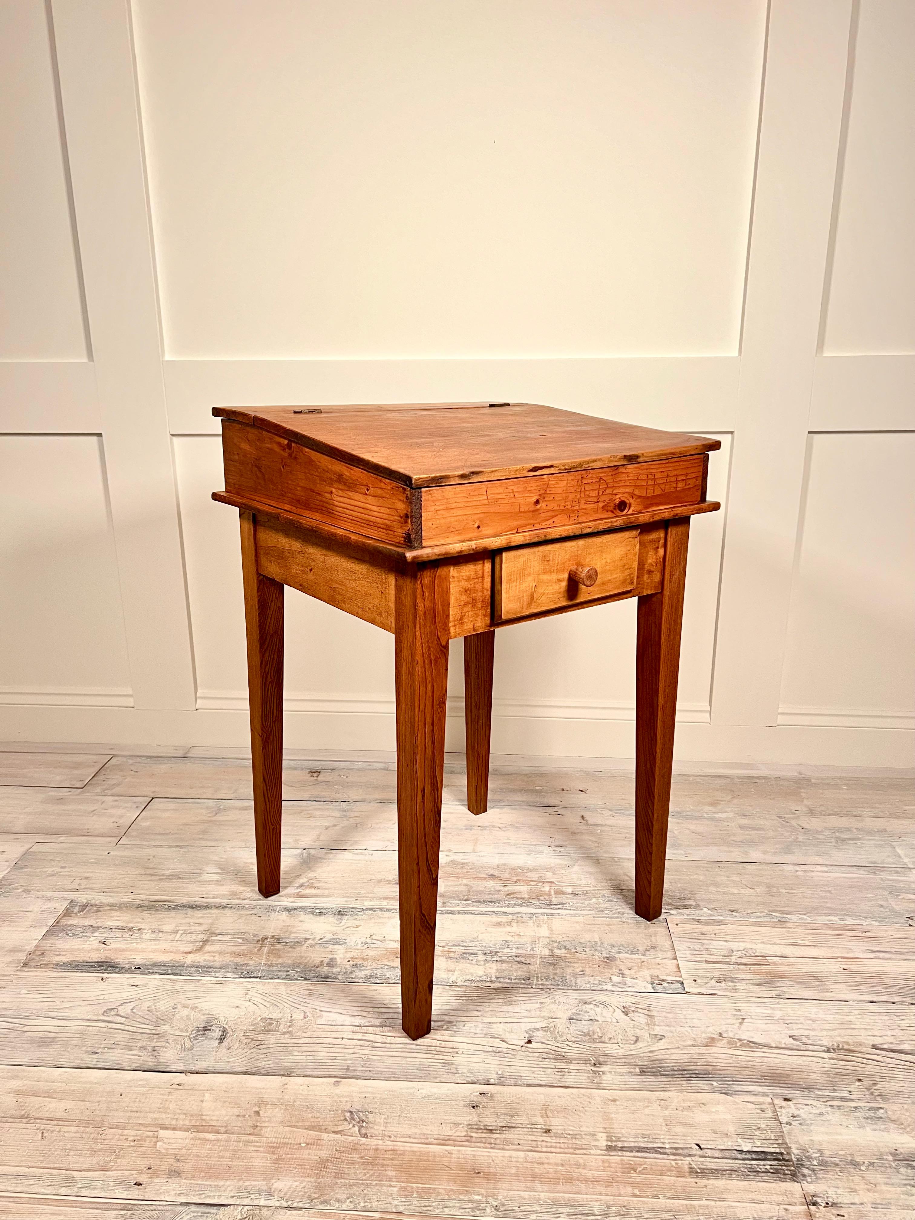 This French 1900's Oak child's school desk is a rare find that exudes immense character. The desk bears the markings of many children who have used it over the years, adding to its charm. Inside the small front drawer and fold-up top storage area,
