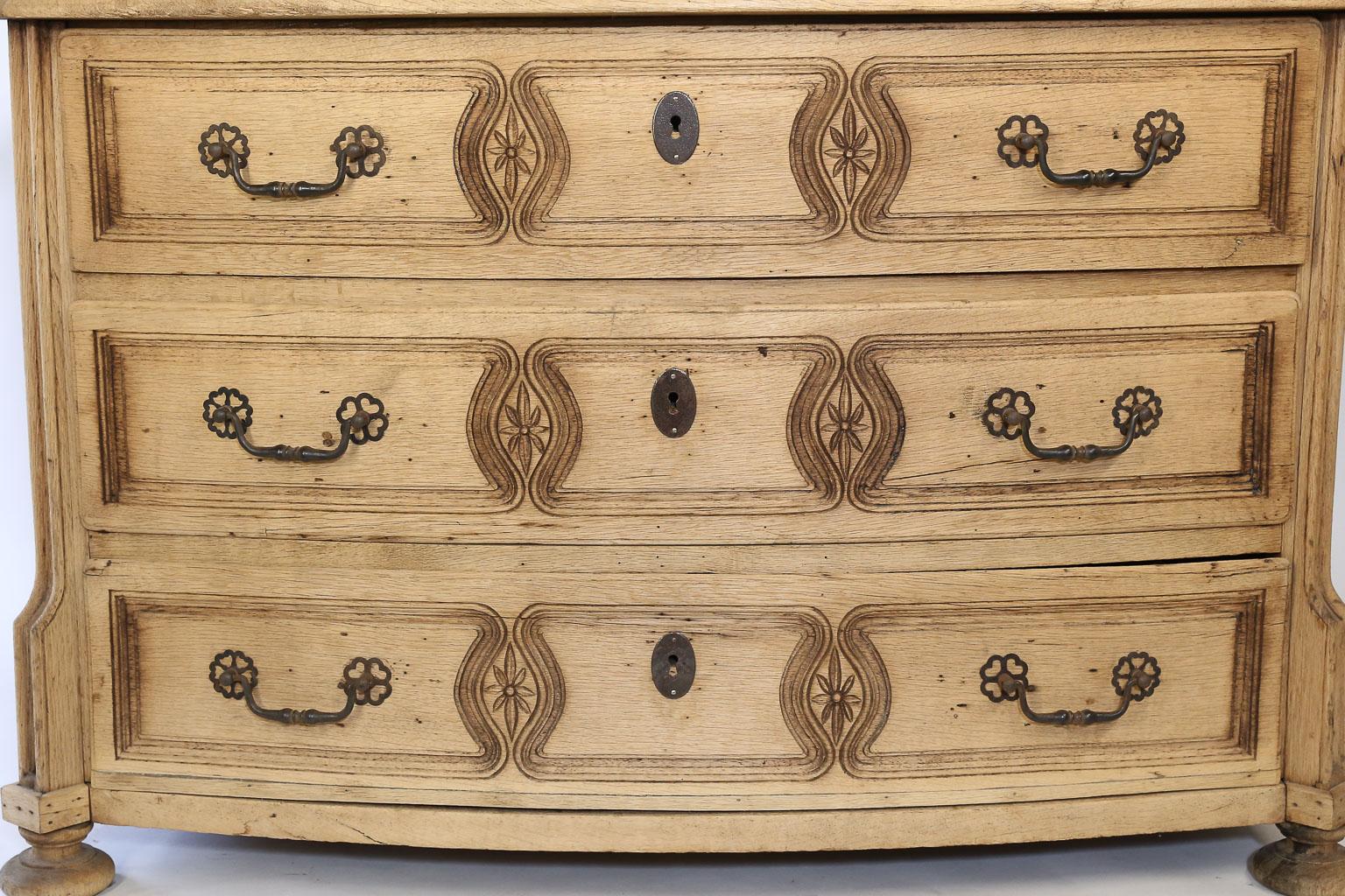 This three-drawer French commode dates to the late 1800s. It has been stripped and bleached which lends to its fabulous patina. Standing on bun feet, each of the three drawers has beautiful carving, two drawer pulls and an iron key hole. The locking