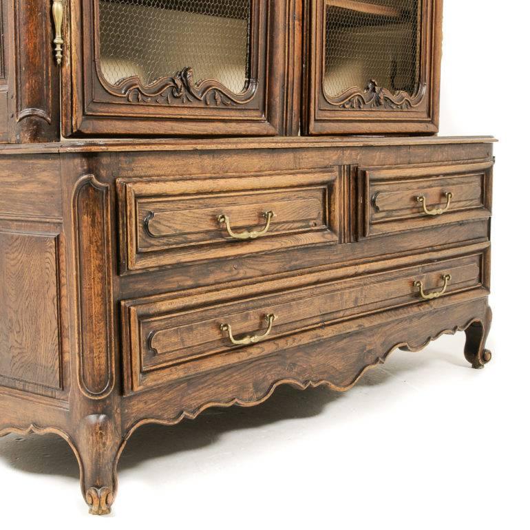 A French, solid oak, ‘deux corps’ vitrine – or display cabinet – with beautiful carved details and ample shelved display in the lit upper section.

The top has two doors fitted with mesh, the bottom is fitted with three drawers, circa
