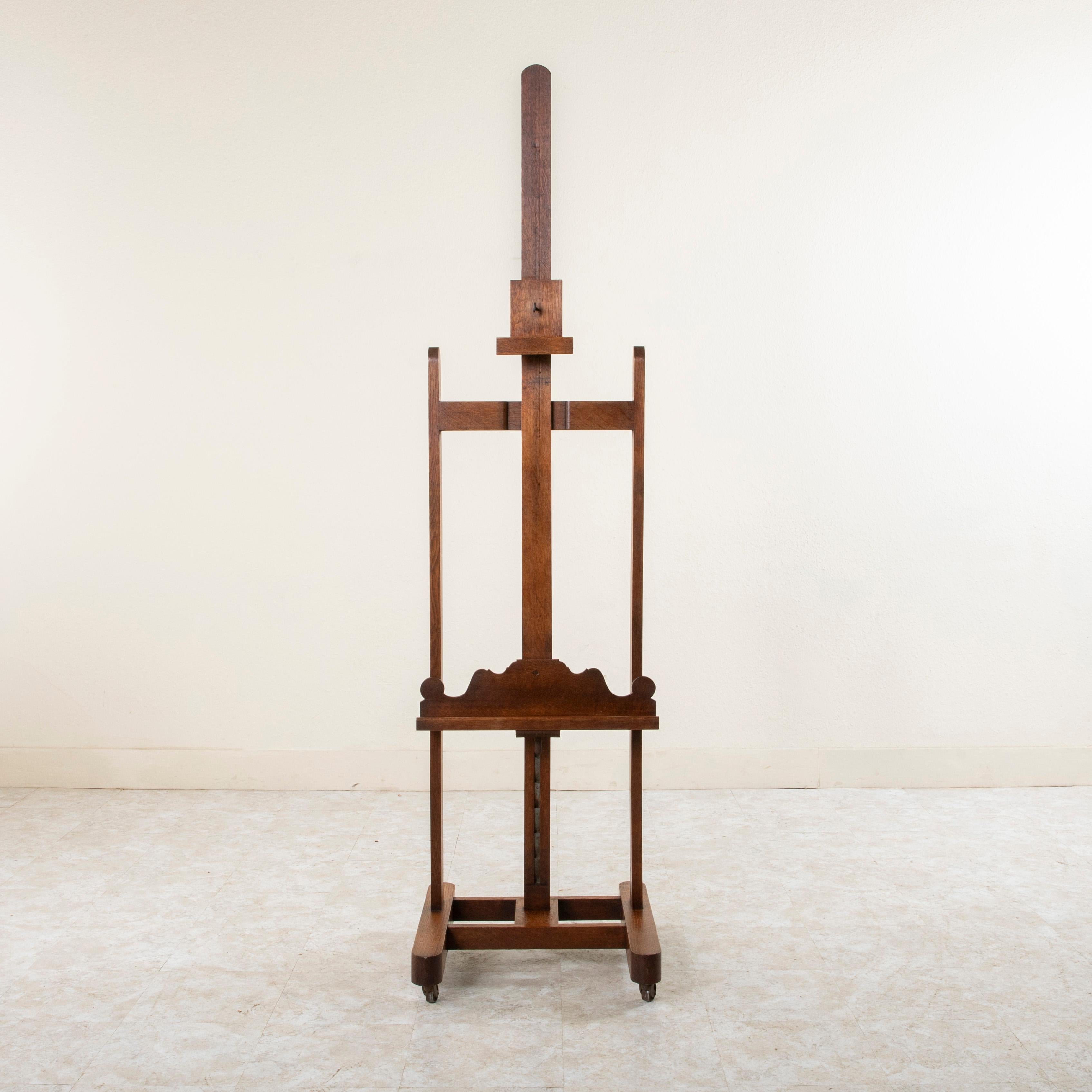 This French oak artist's floor easel from the turn of the twentieth century features iron casters and an iron pull lever mechanism that allows for an adjustable height of 67 to 102 inches. Its 3.5 inch deep tray allows for larger canvases to be