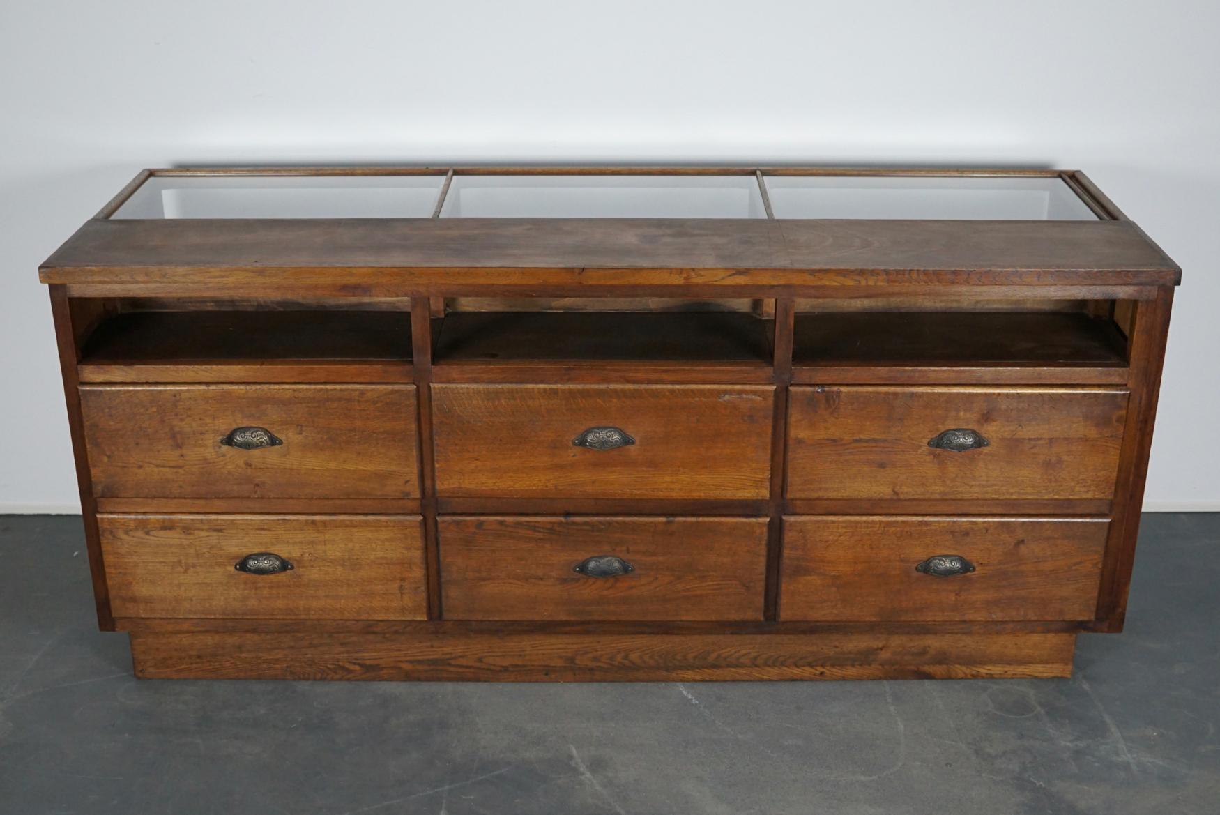 This vintage oak haberdashery shop counter dates from the 1930s and was made in France. It features a solid wooden frame and drawers in oak with brass handles.