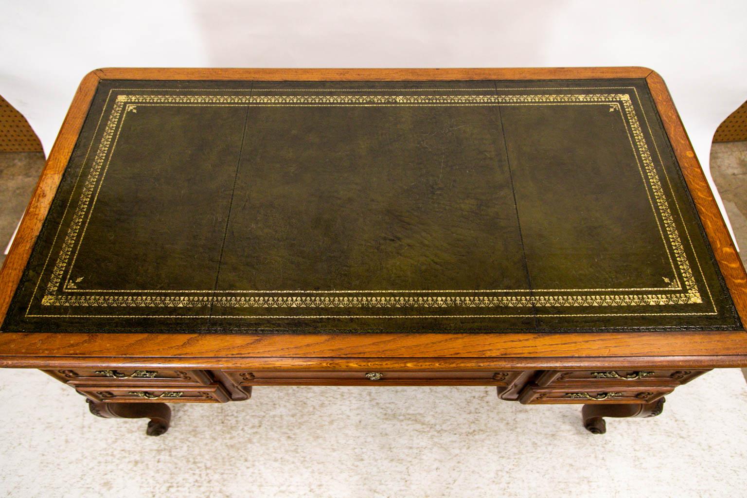 Questa scrivania è realizzata in un bellissimo rovere francese ed è rifinita sul retro e sui lati con pannelli in rilievo. La parte superiore in pelle è di colore verde oliva con dettagli dorati.