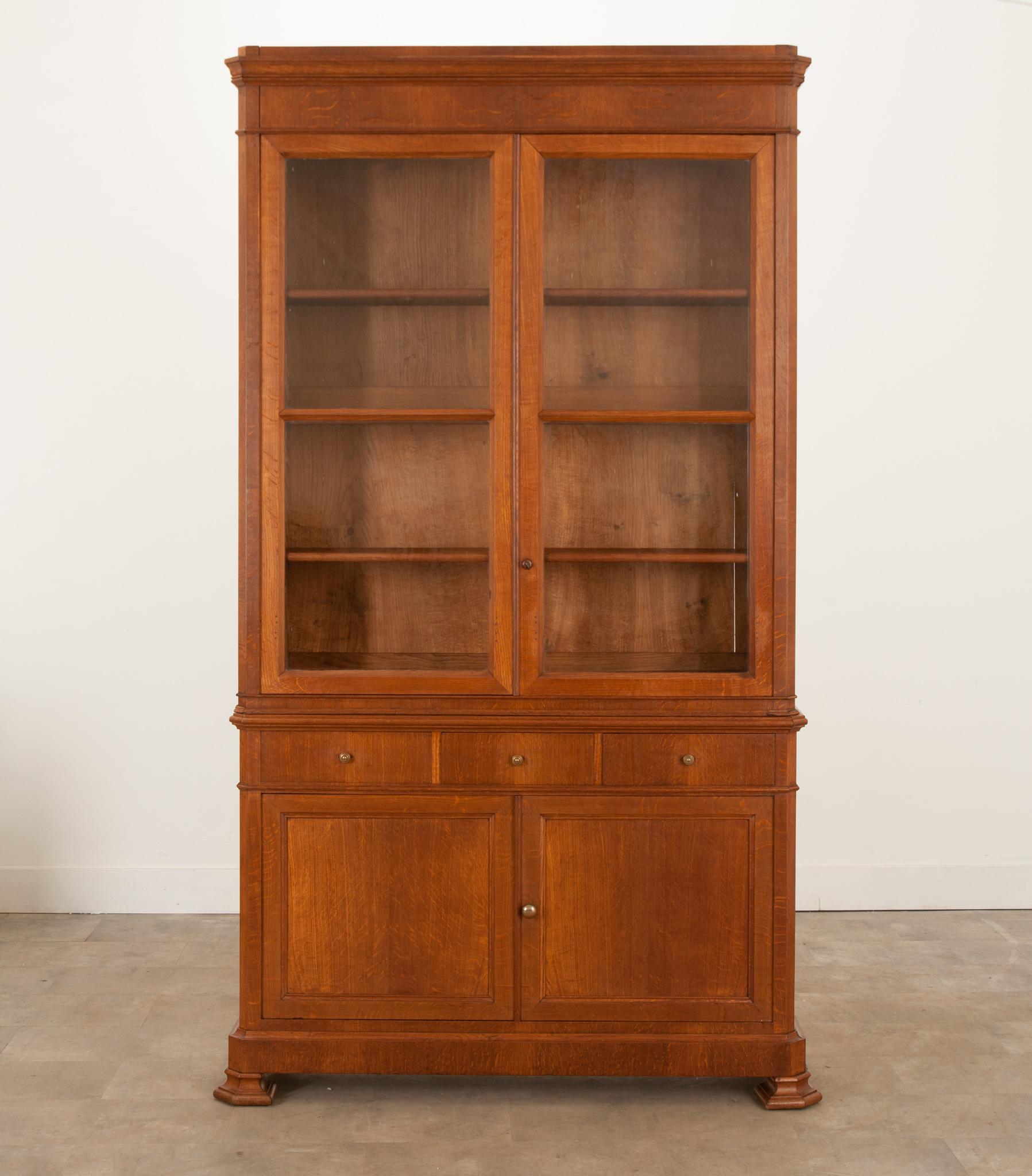 A fantastic French Louis Philippe style bibliotheque, finished in beautiful, quarter sawn oak, circa 1860. This uniquely shallow bookcase has an upper portion, outfitted with three adjustable shelves, set behind doors that contain their original