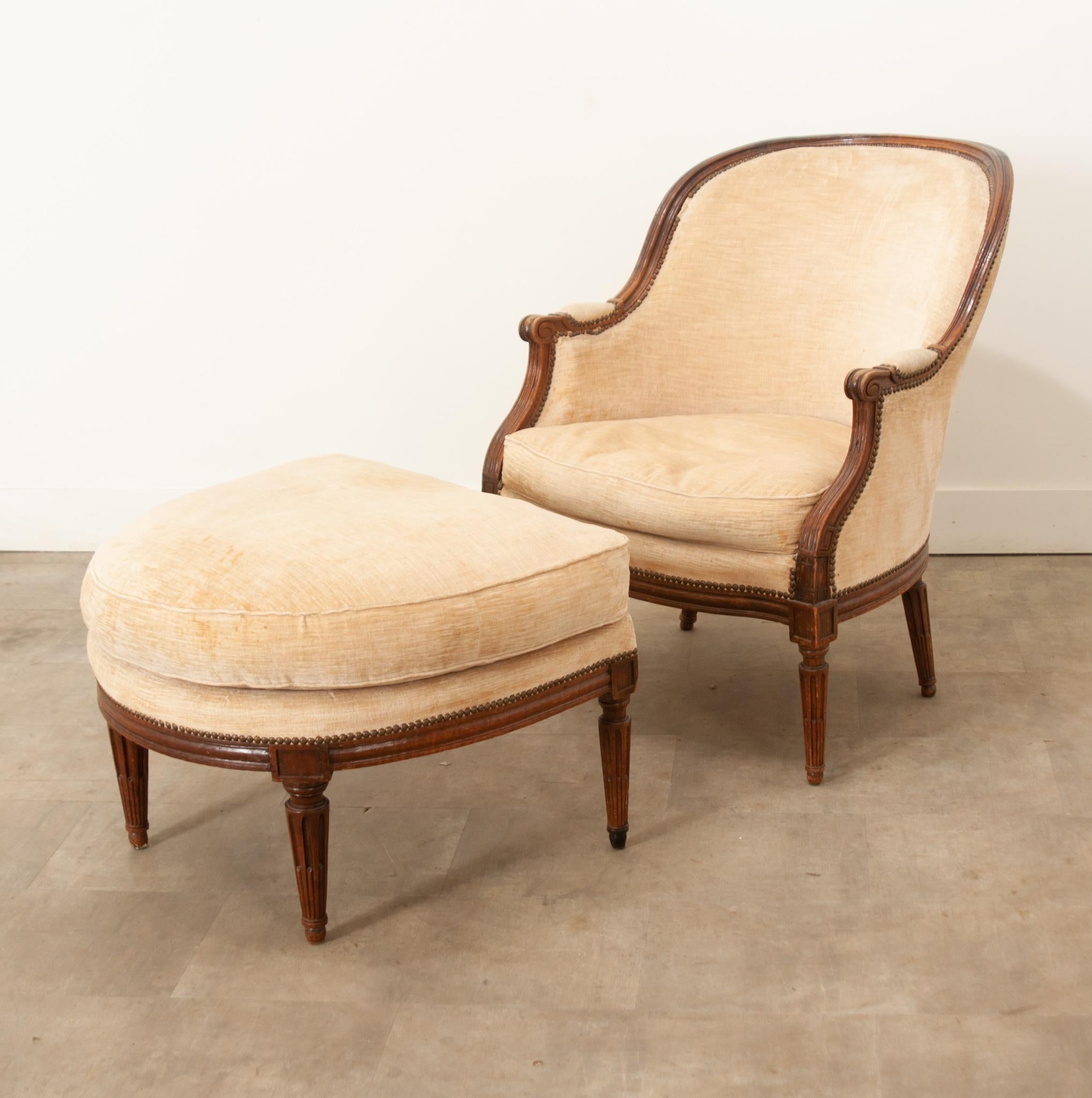 A sophisticated set that includes a French 19th century oak bergere and ottoman. Fluted legs, indicative of the Louis XVI style, support each broad cushioned piece with slender elegance. The sturdy oak frames of each are deeply carved, molded and