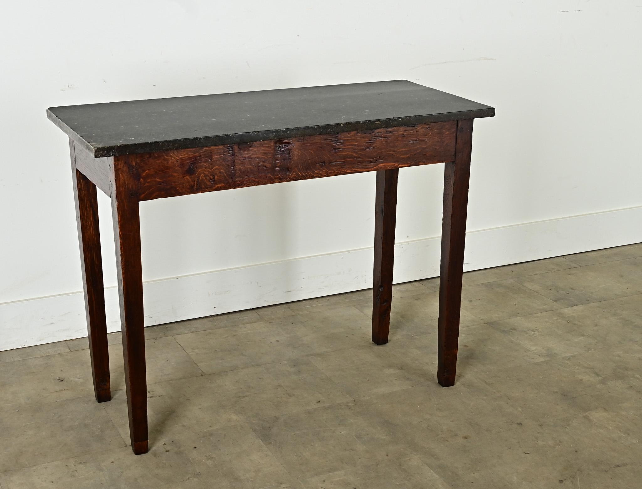 Crafted in France circa 1850, this unique console table is topped with a dark slab of hand-cut marble featuring inclusions of tiny fossils. In the apron one can see the joinery technique of wooden pegs. The wonderfully patinated hardwood apron is