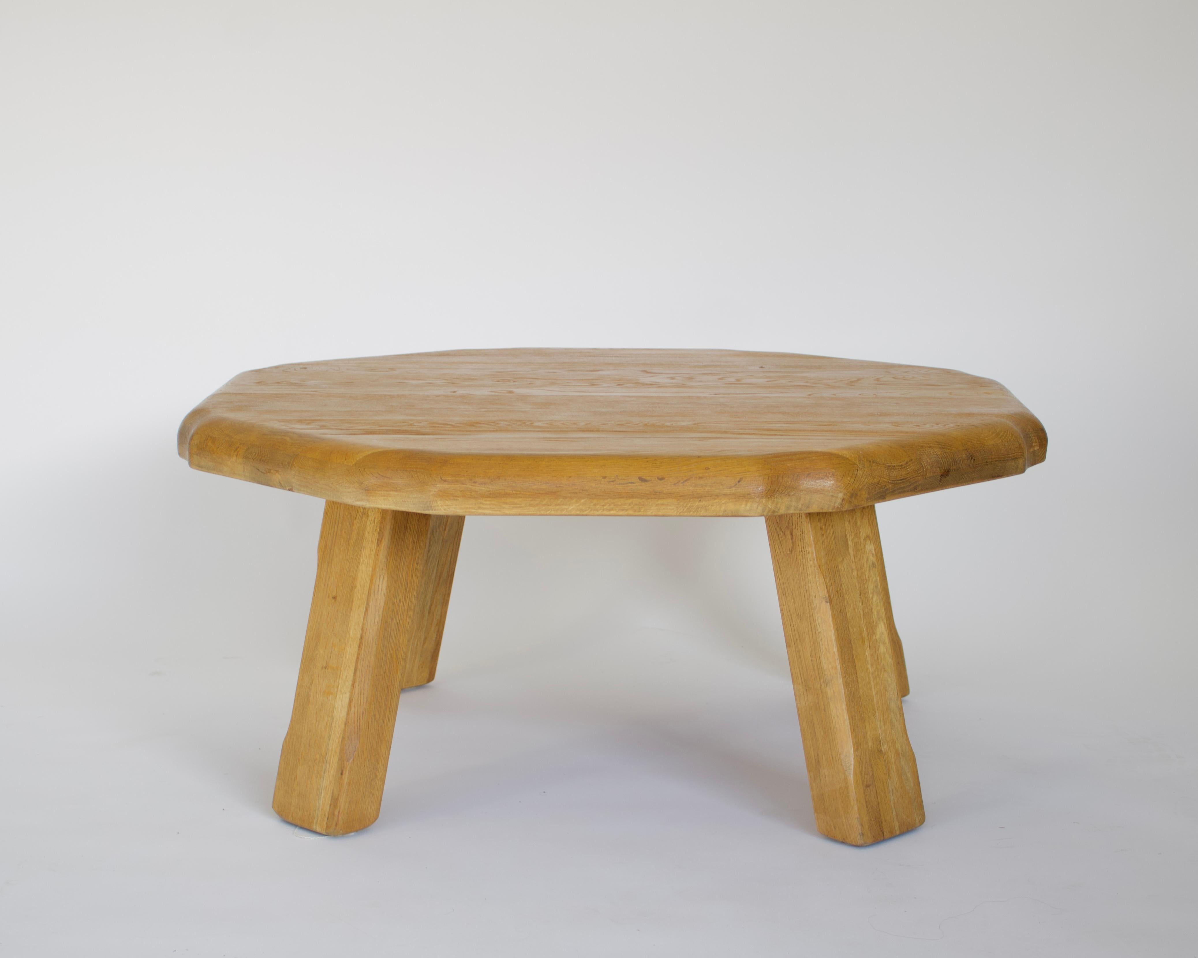 French round with asymmetrical carved edge honey colored oak coffee table from the 1960's. 
The table is composed of 6 laminated layers of French oak, each showcasing a different grain of the wood. The massive legs also are composed of laminated