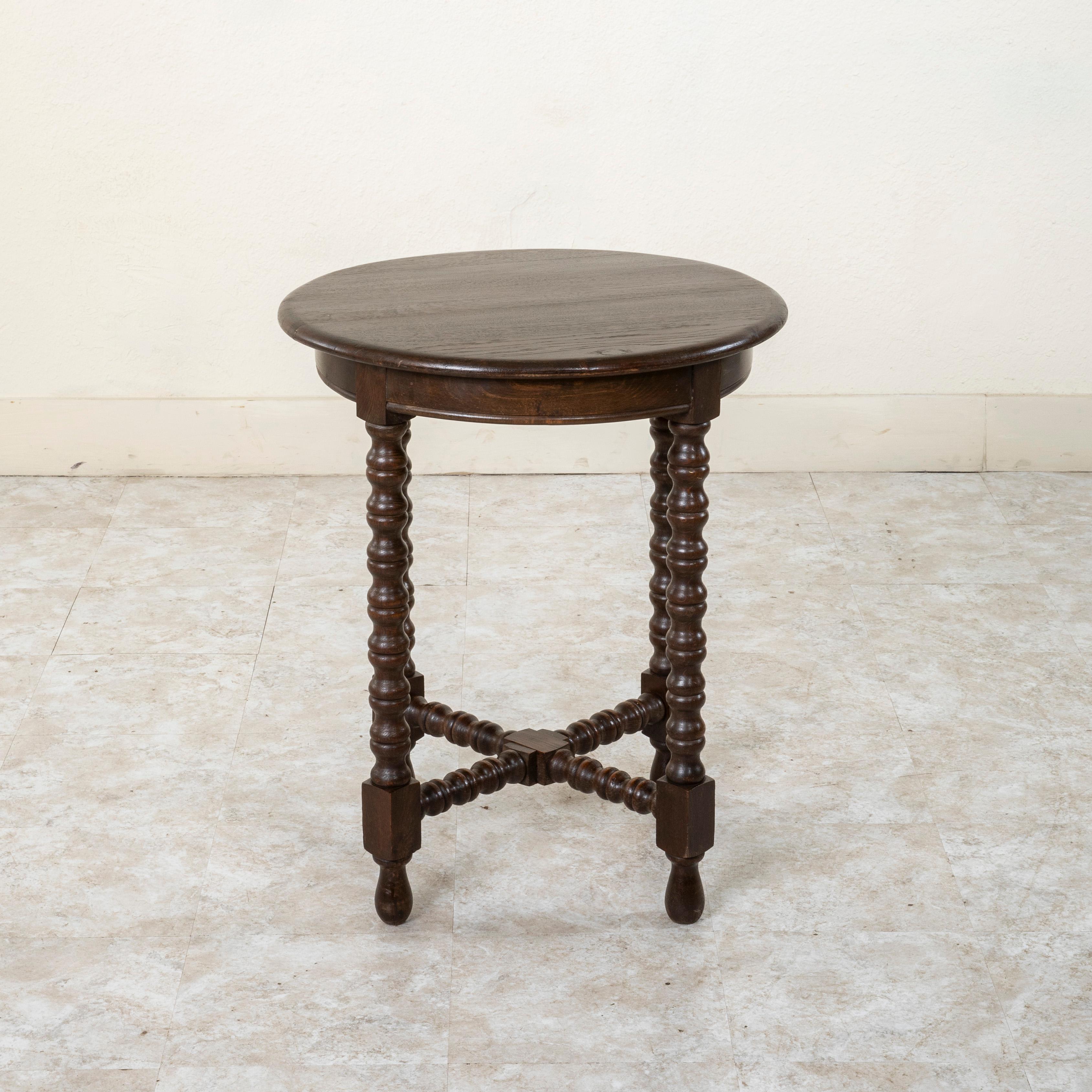 This French oak side table from the turn of the twentieth century features four turned legs joined by a lower X stretcher. Its sturdy base supports a 23.5 inch diameter beveled top. A handsome table to place beside a chair or between two chairs. c.