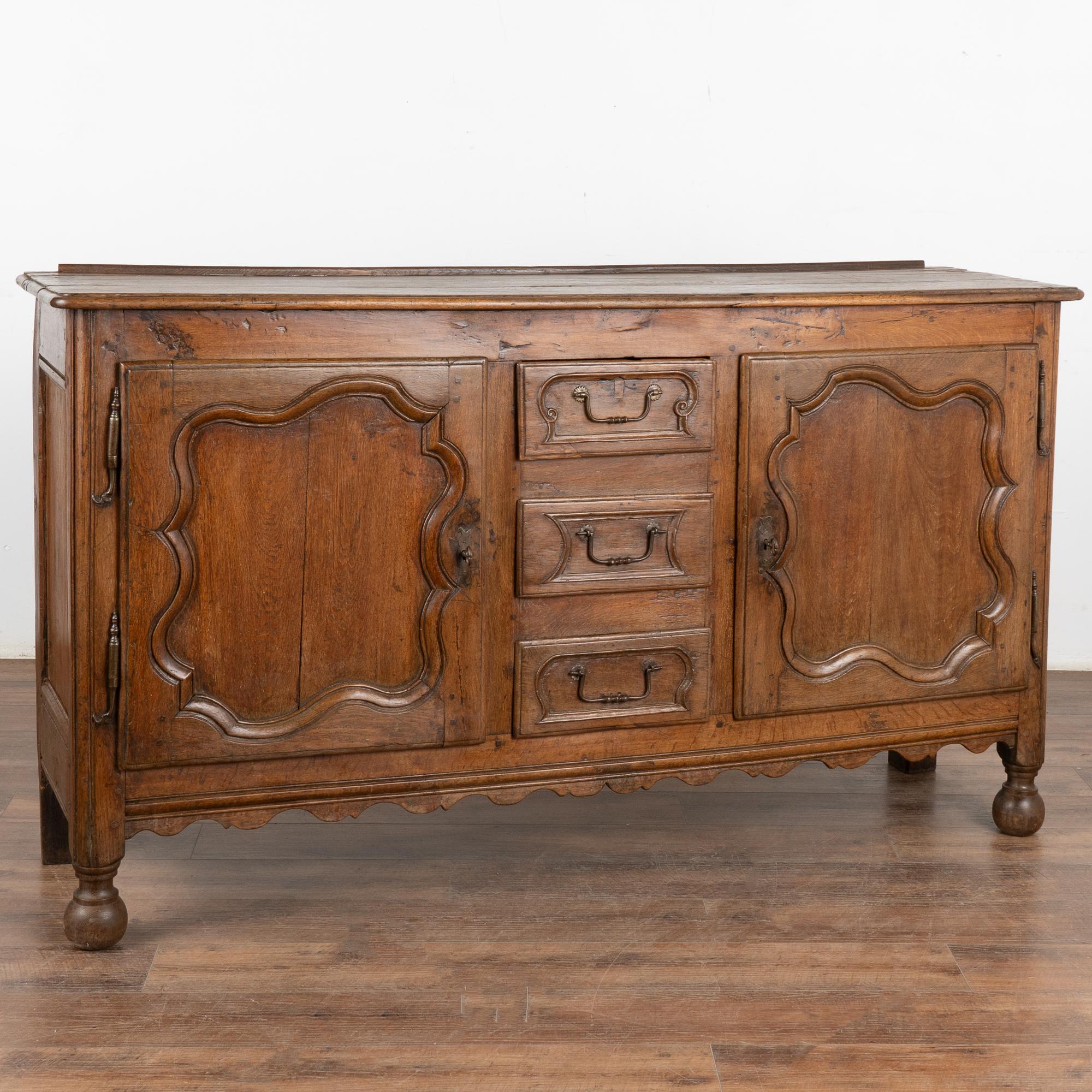 French oak sideboard with traditional carved panel details and scalloped skirt. The deep, rich patina of the wood reflects generations of use. At just under 6' long, this will serve well as a buffet or console. 
Restored, strong, stable and ready