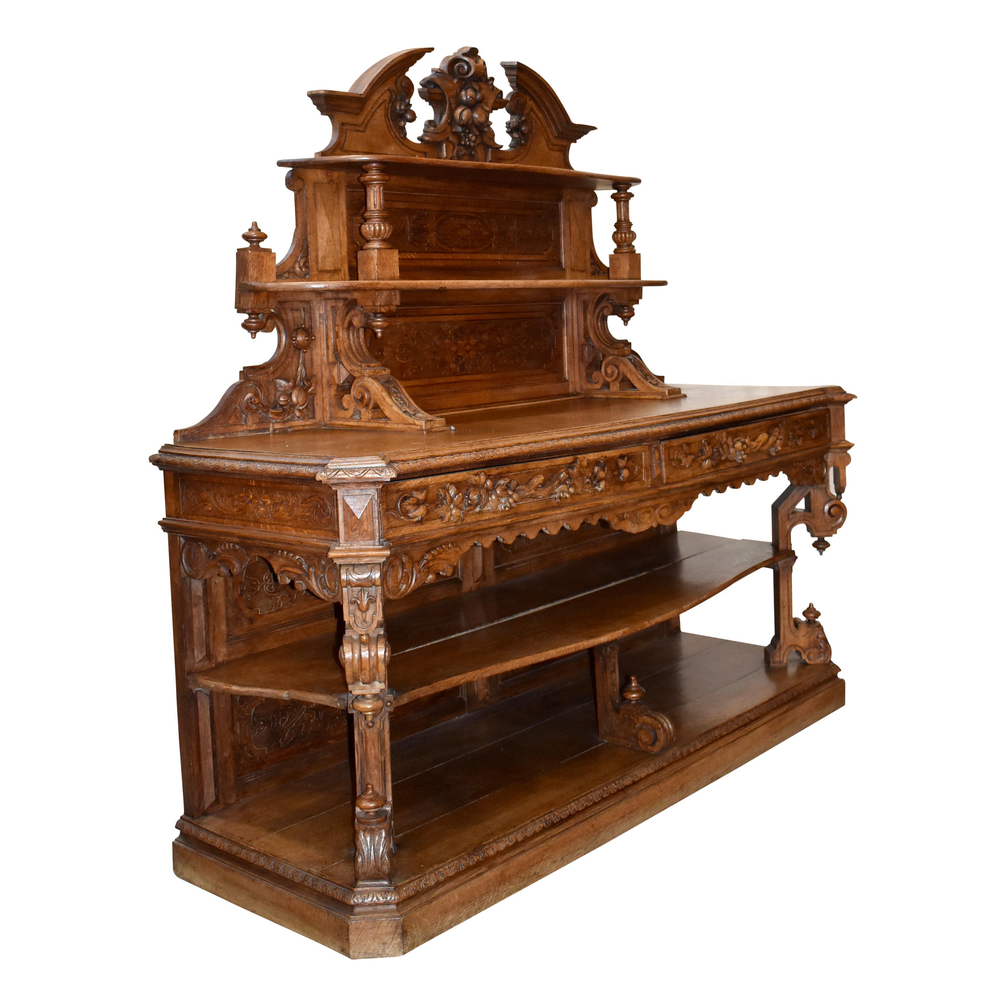 A luxurious piece with extensive carving, this seven foot oak sideboard from France features an open design with three serpentine shelves. A broken pediment with a central carving of fruit nestled in leaves crowns the top over two upper shelves. The