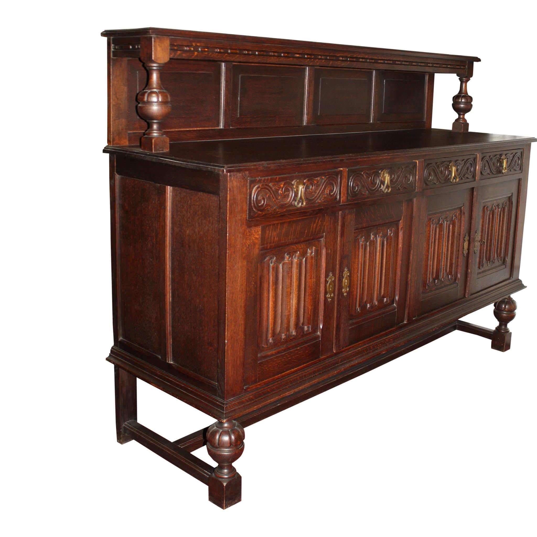 Constructed of solid oak with a beautiful, dark finish, this French sideboard features four doors with linenfold carvings and brass escutcheons, four drawers with brass, pendant pulls flanked by horizontal S scrolls, and a backboard of four raised