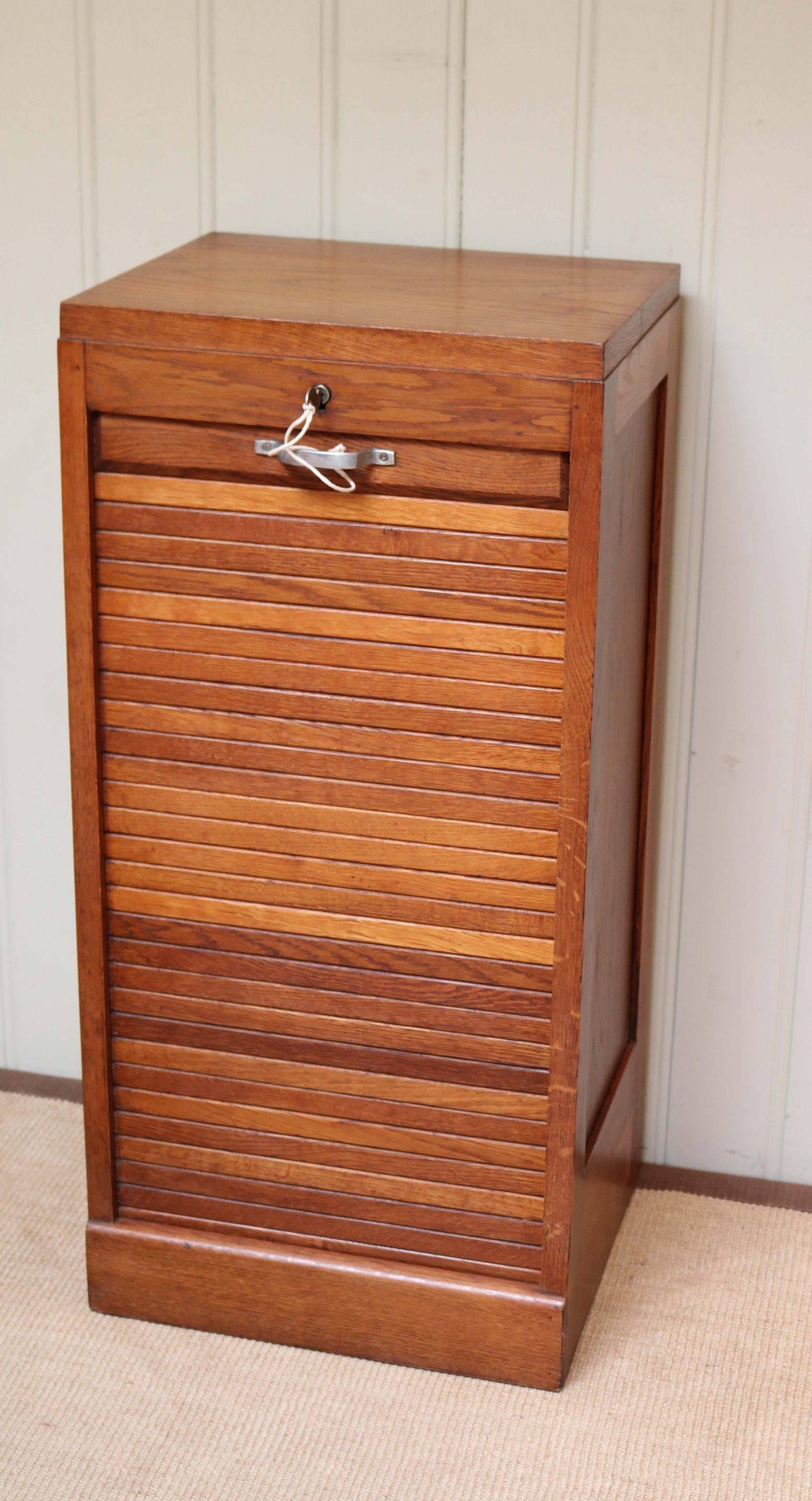 French oak single tambour front filing cabinet having five fixed plywood shelves which slide, raised on a plinth base.