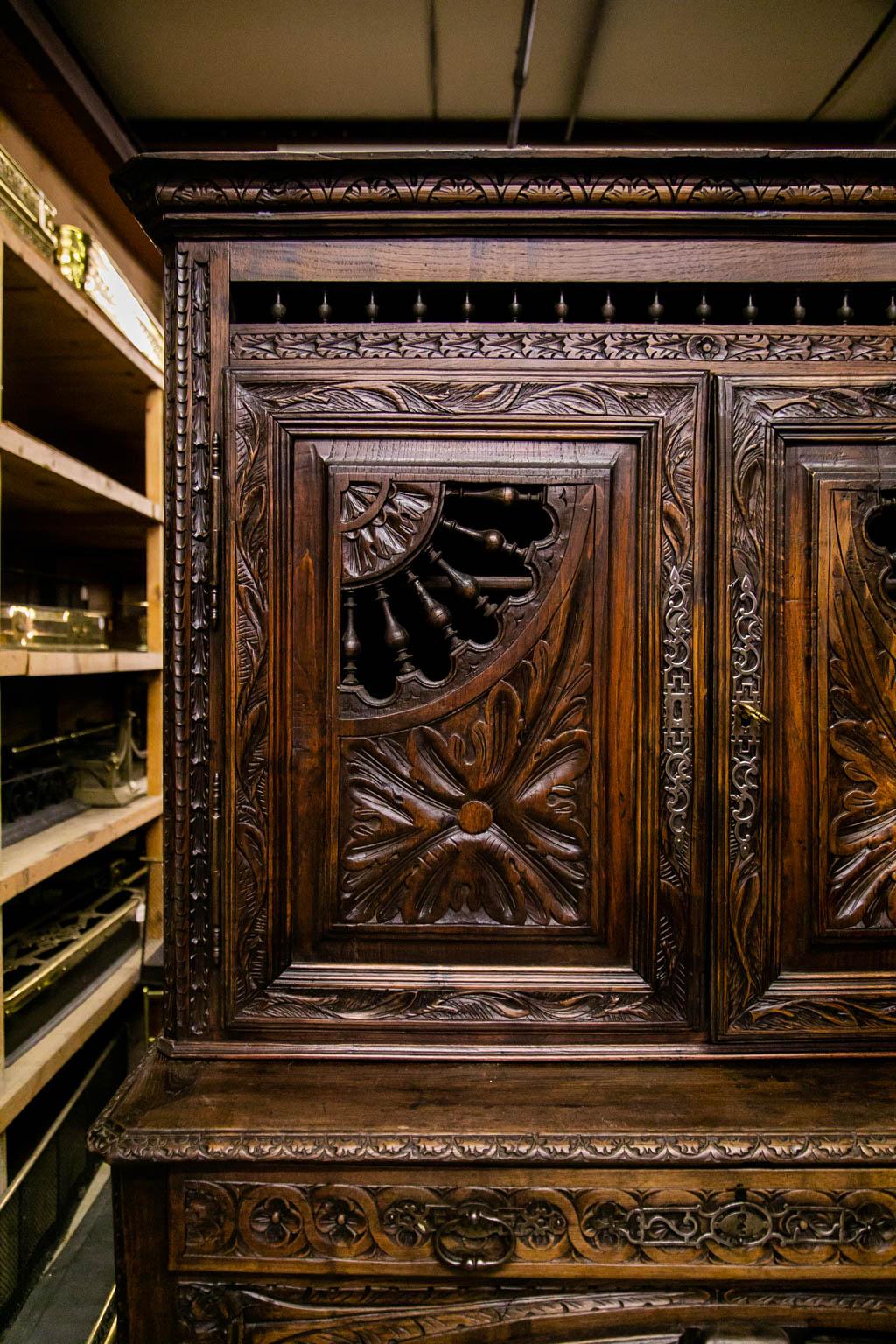 This cupboard is profusely carved overall with stylized leaves and repeating stylized ribbons. It retains its original large intricate steel fretwork escutcheons. The upper doors are carved with open quarter wheel balustrades. The large steel hinges