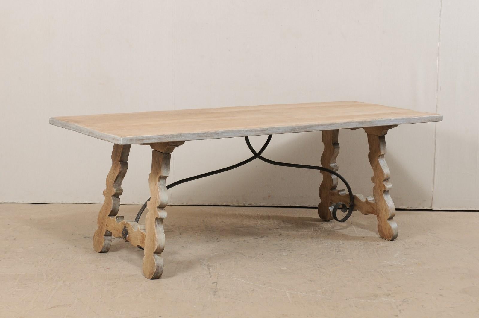 A French oak trestle table with iron stretcher from the mid-20th century. This vintage table from France features a rectangular shaped top, just over 7 feet in length, raised upon a pair of fluidly-carved trestle legs, which tops tilt slightly