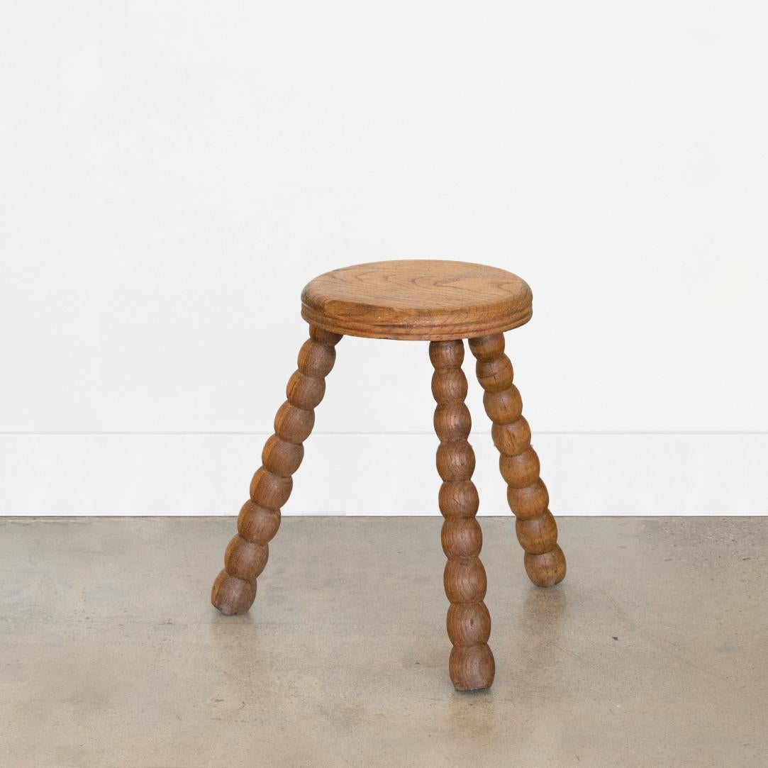 Vintage oak tripod stool with beautiful bobbin legs from France. Circular seat with original light oak finish showing great age markings and patina. Circular top with small flat edge on one side. Can be used as small stool or as side table next to