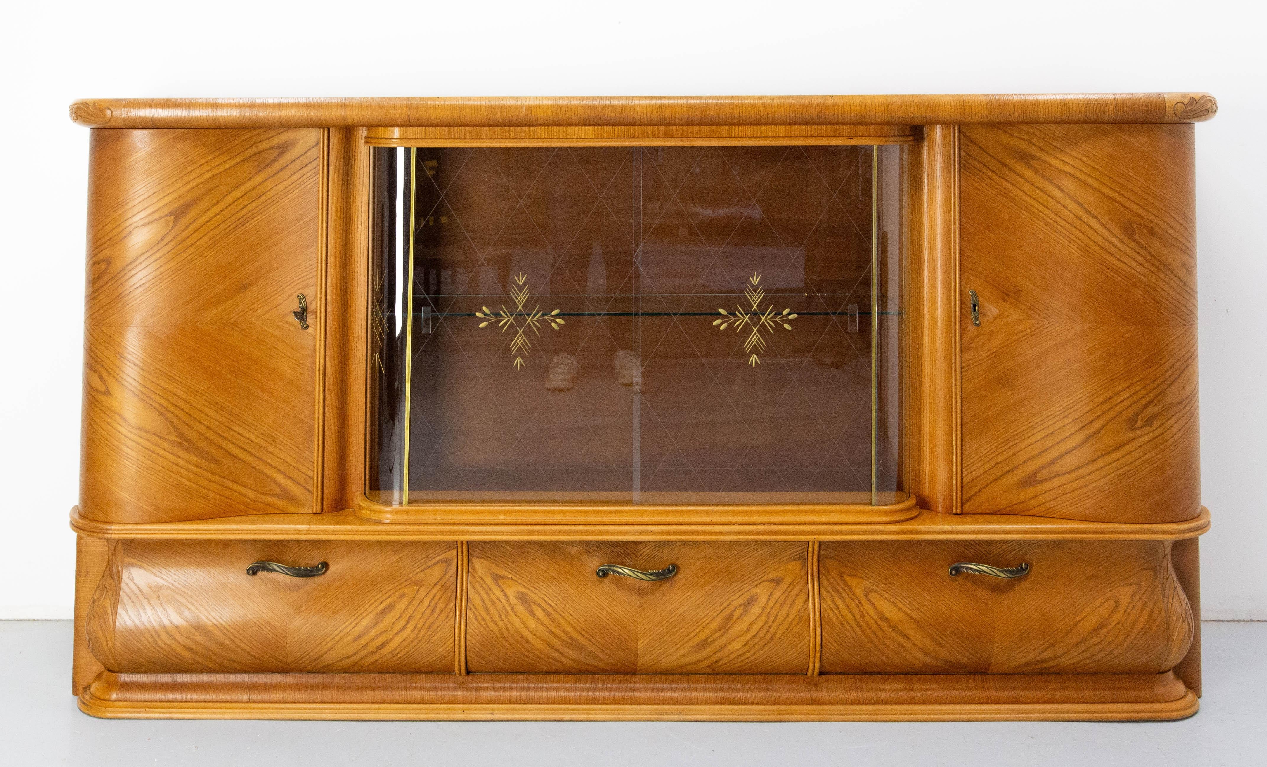Armario de pared de un bufé de dos piezas. 
Roble, cristal y latón.
Este mueble es todo curvas, hasta el cristal, lo que lo hace muy original.
Estilo típico de los años 50, meticulosamente elaborado.
Mucho espacio de almacenamiento en un espacio