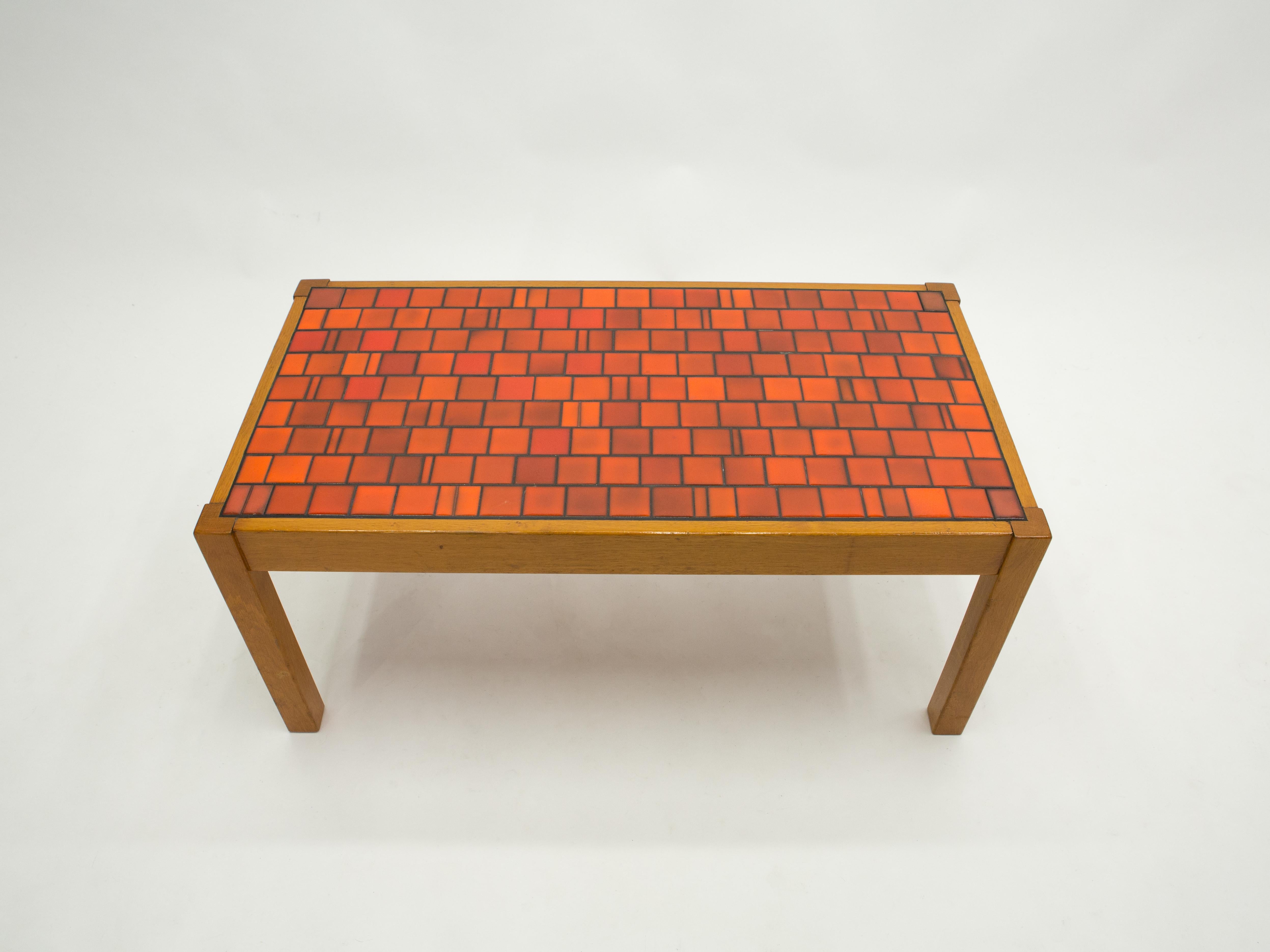 This beautiful French ceramic coffee table is typical 1960s, with its solid oak wood base and shades of red ceramic tales. The ceramic table surface explodes with warm color from rust red to hot orange, forming an eye-catching pattern across the