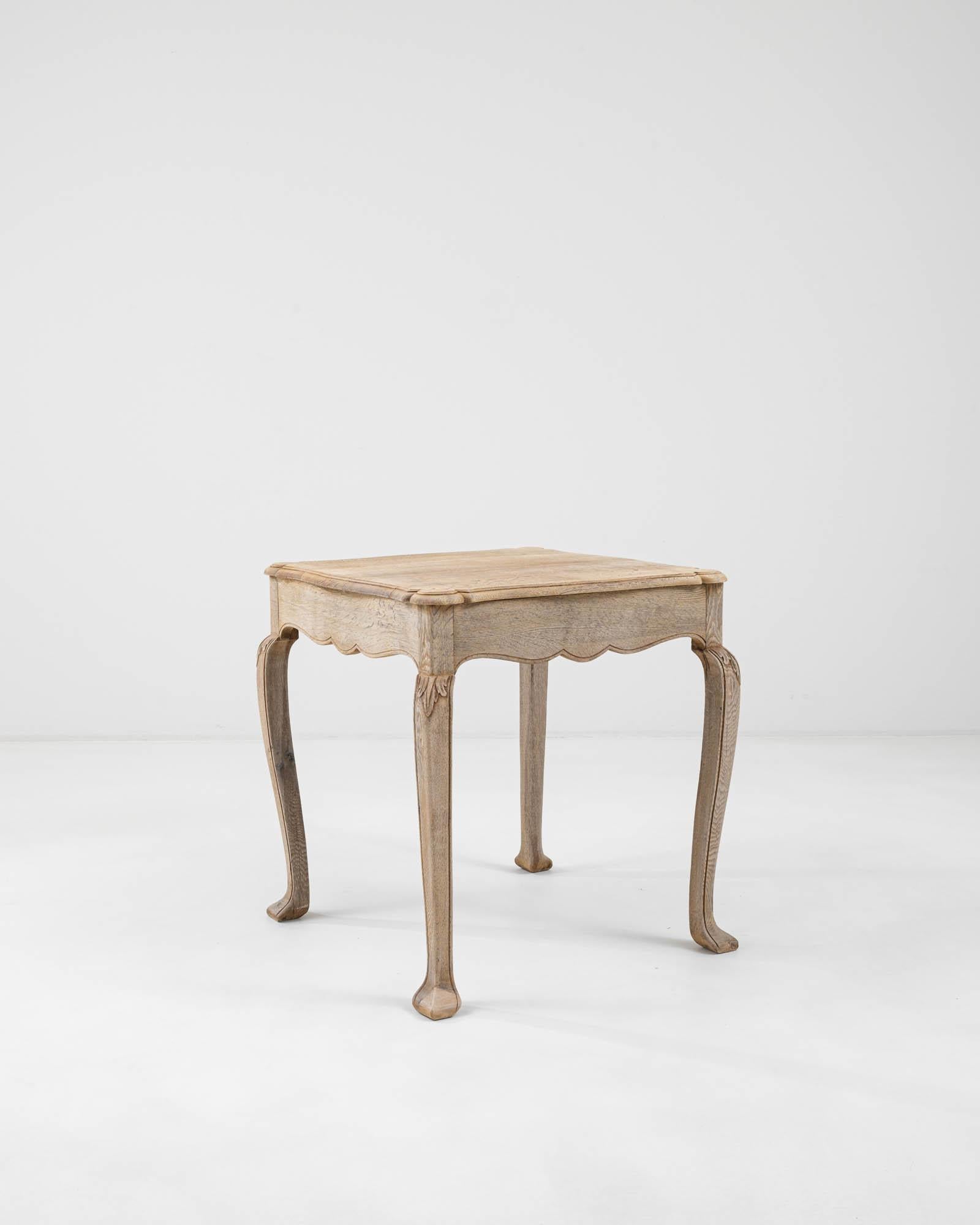An antique bleached oak table from France with distinctive curved legs. Stylish and practical with a versatile shape, four limbs stretch to support the scalloped apron and a softly beveled tabletop. 
Perched on cabriole legs – the piece imparts a