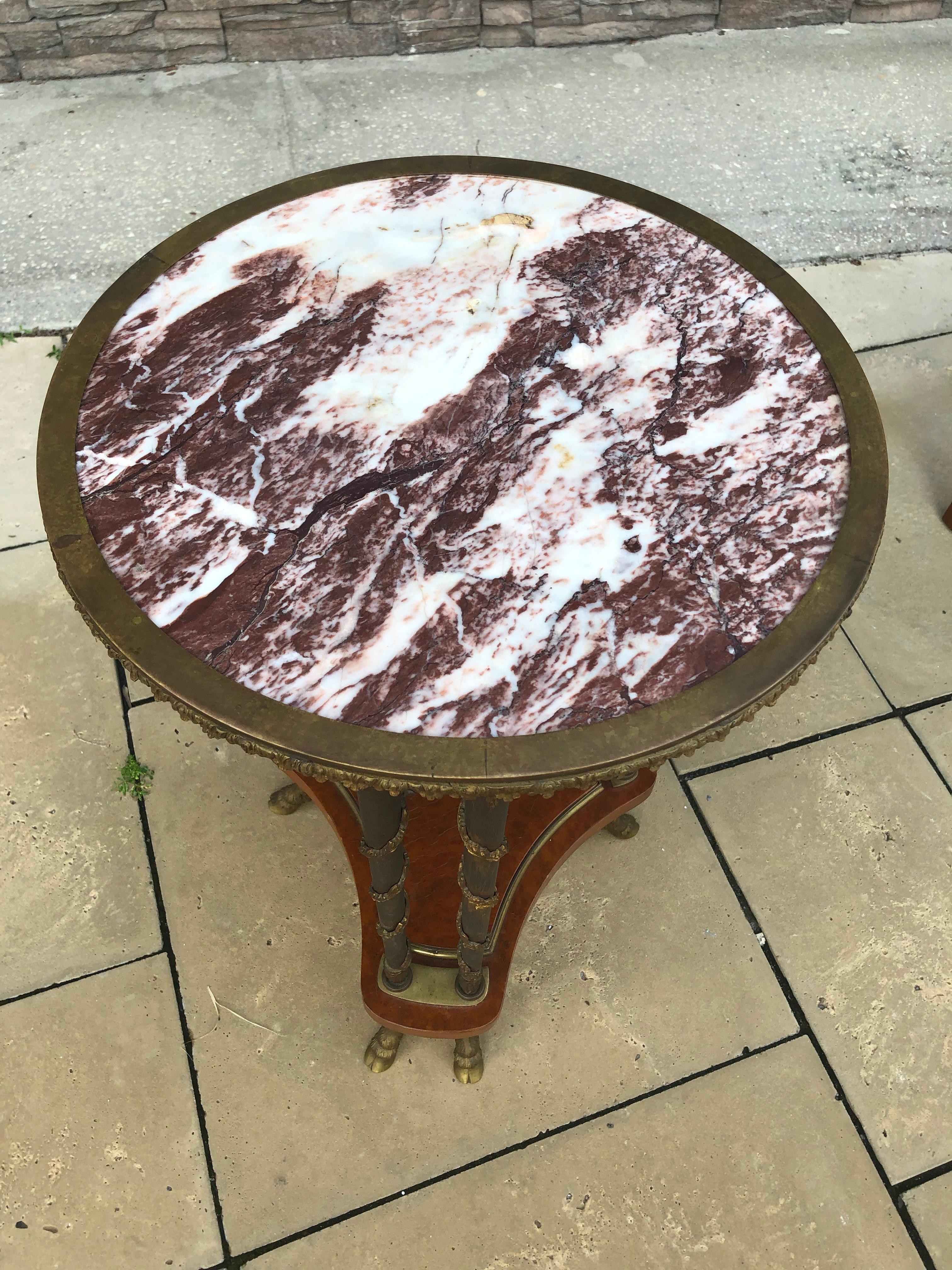 This table has a marble top in rouge and cream banded in a scalloped bronze two legs together (3 legs total) having bronze garland twist another each column shelve to the bottom ending with 