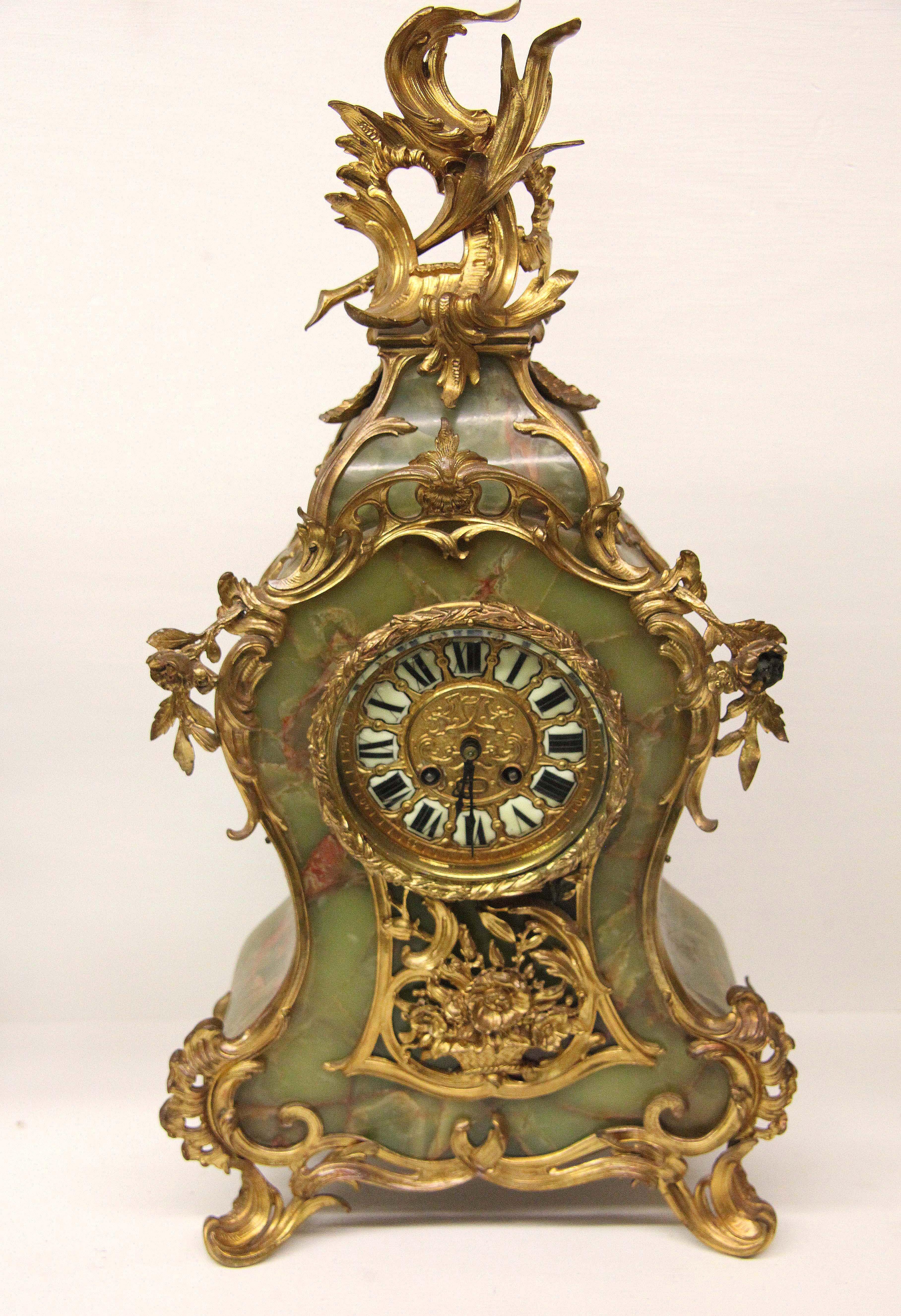 French onyx serpentine clock set, with serpentine shaped sides, the front decorated with ormolu featuring floral and foliate. The dial with porcelain Roman numerals inside beveled glass bezel above elaborate floral and foliate ormolu. The matching