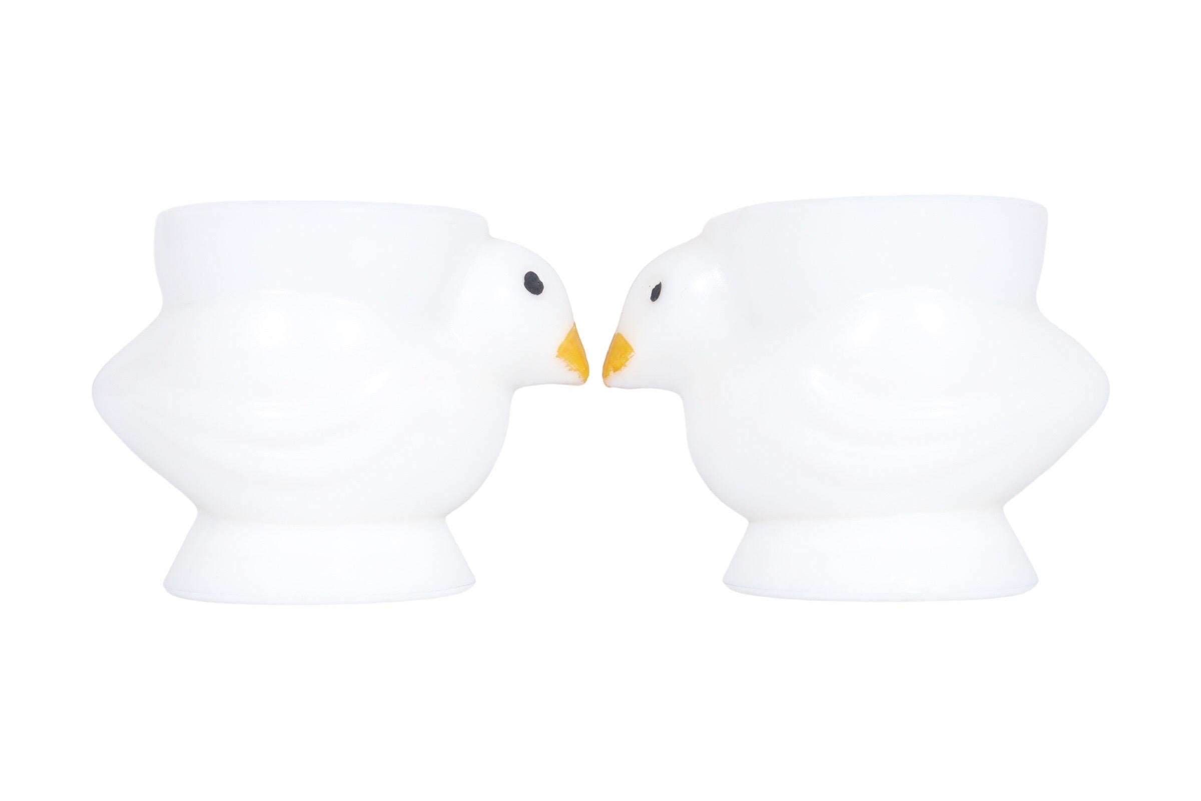 A pair of French Opalex white chick egg cups. Shaped like chicks with lines detailing the wings and head. Beaks are painted yellow, and eyes are dotted in black. Marked France Opalex underneath. Dimensions per egg cup.
 
