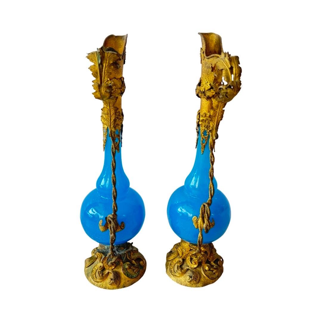 A refined 19th-century French vanity set crafted in vibrant opaline blue glass, richly adorned with ornate gilt bronze mounts in the Rococo Revival style, typical of the Napoleon III period (circa 1860–1880). The set consists of two tall ewers, a